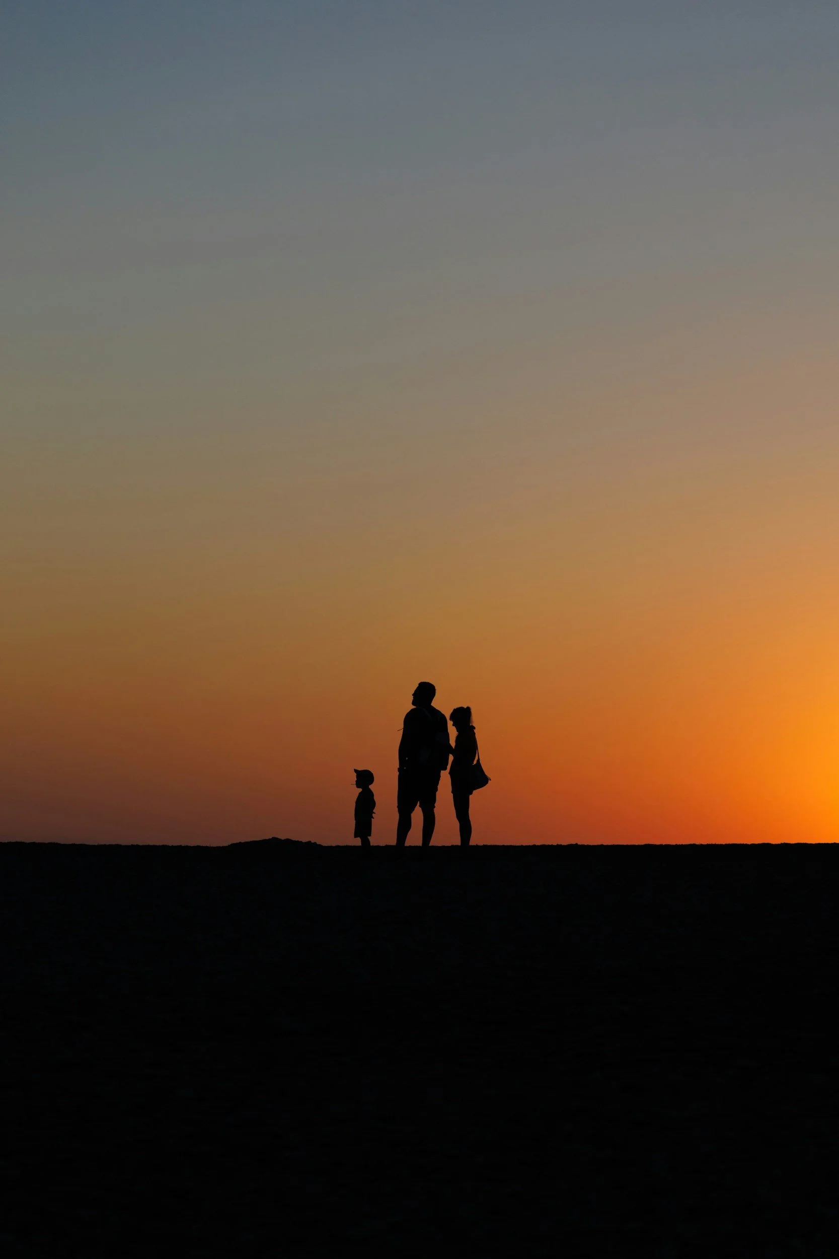 Silhouettes of a man, woman, and two children standing on a hill at sunset, with a colorful sky in the background.