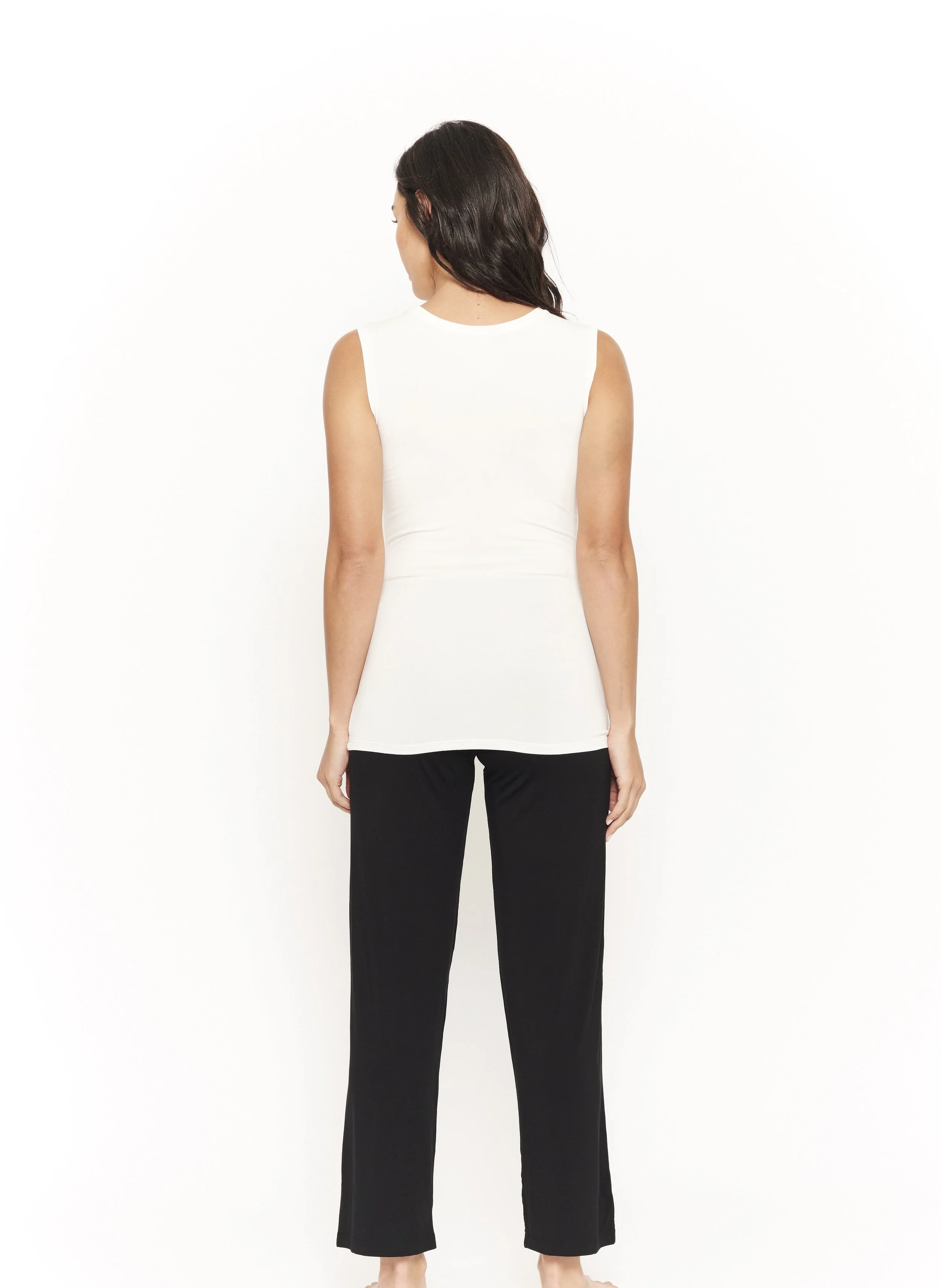 Woman with long black hair standing in relaxed position wearing a cream tank top and flowing black pants