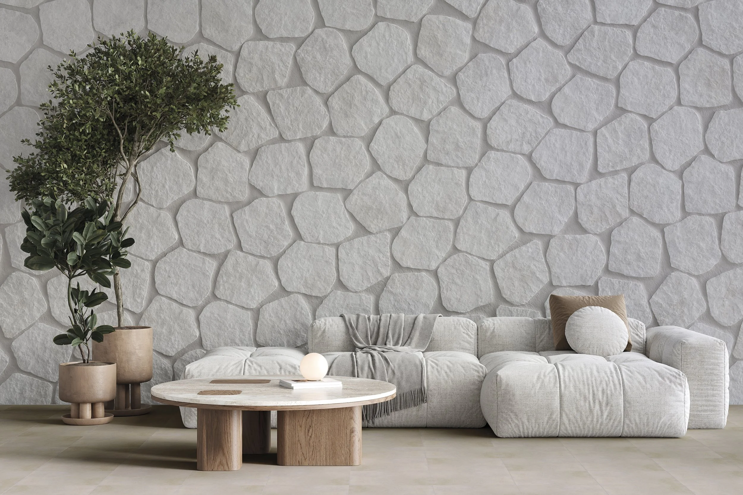 Salon moderne avec mur en pierre blanche, canapé beige, coussin beige, table basse ronde en bois, deux grands pots avec plantes vertes, lampe bout de bois