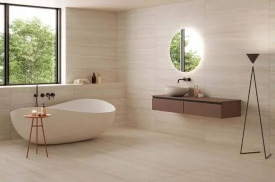 Salle de bain moderne avec une baignoire autoportante, un lavabo sur un meuble suspendu, un miroir rond, une grande fenêtre avec vue sur des arbres, et un lampadaire noir.