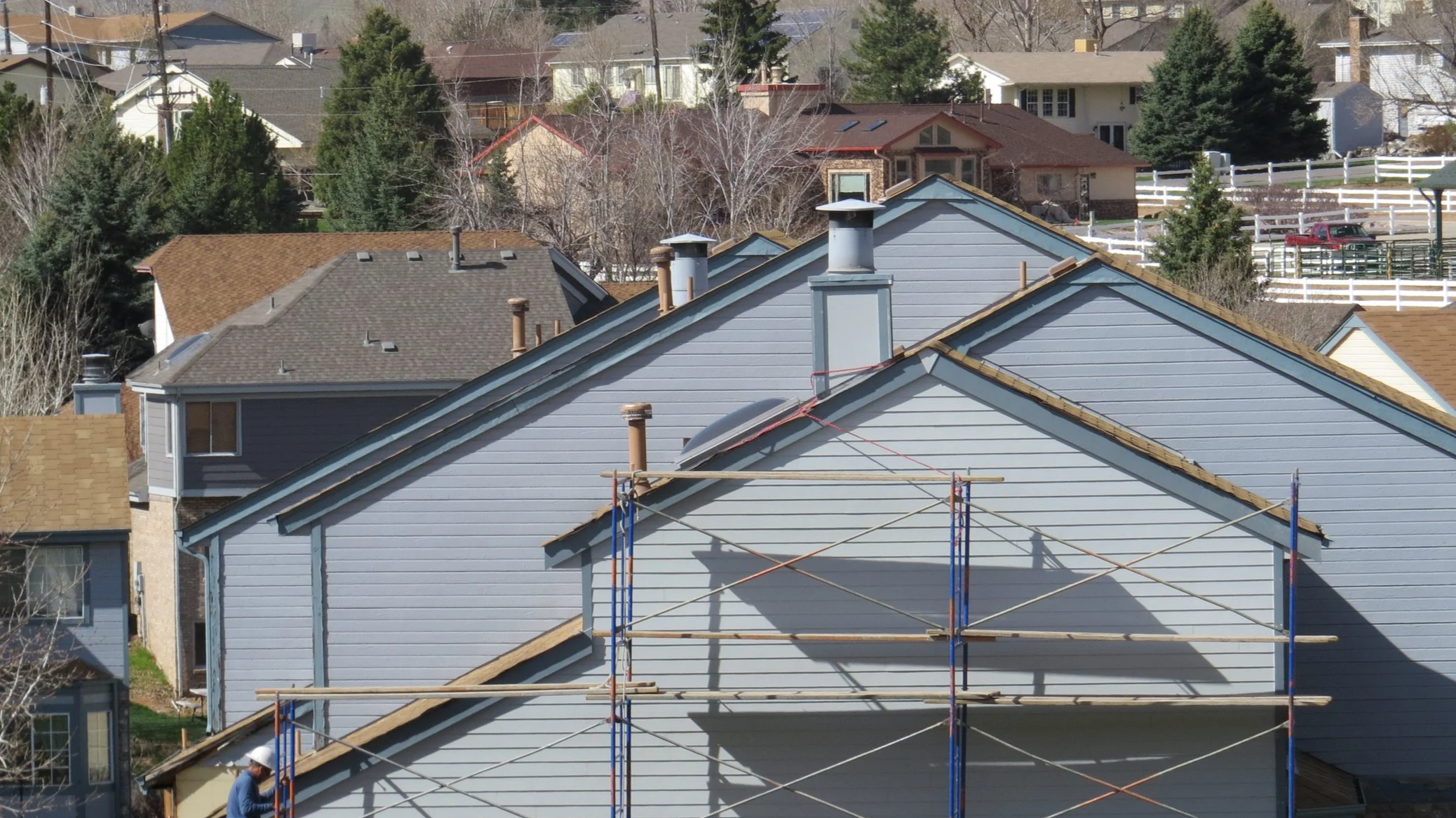 Residential neighborhood with houses, trees, and a construction scaffold on a house's roof.