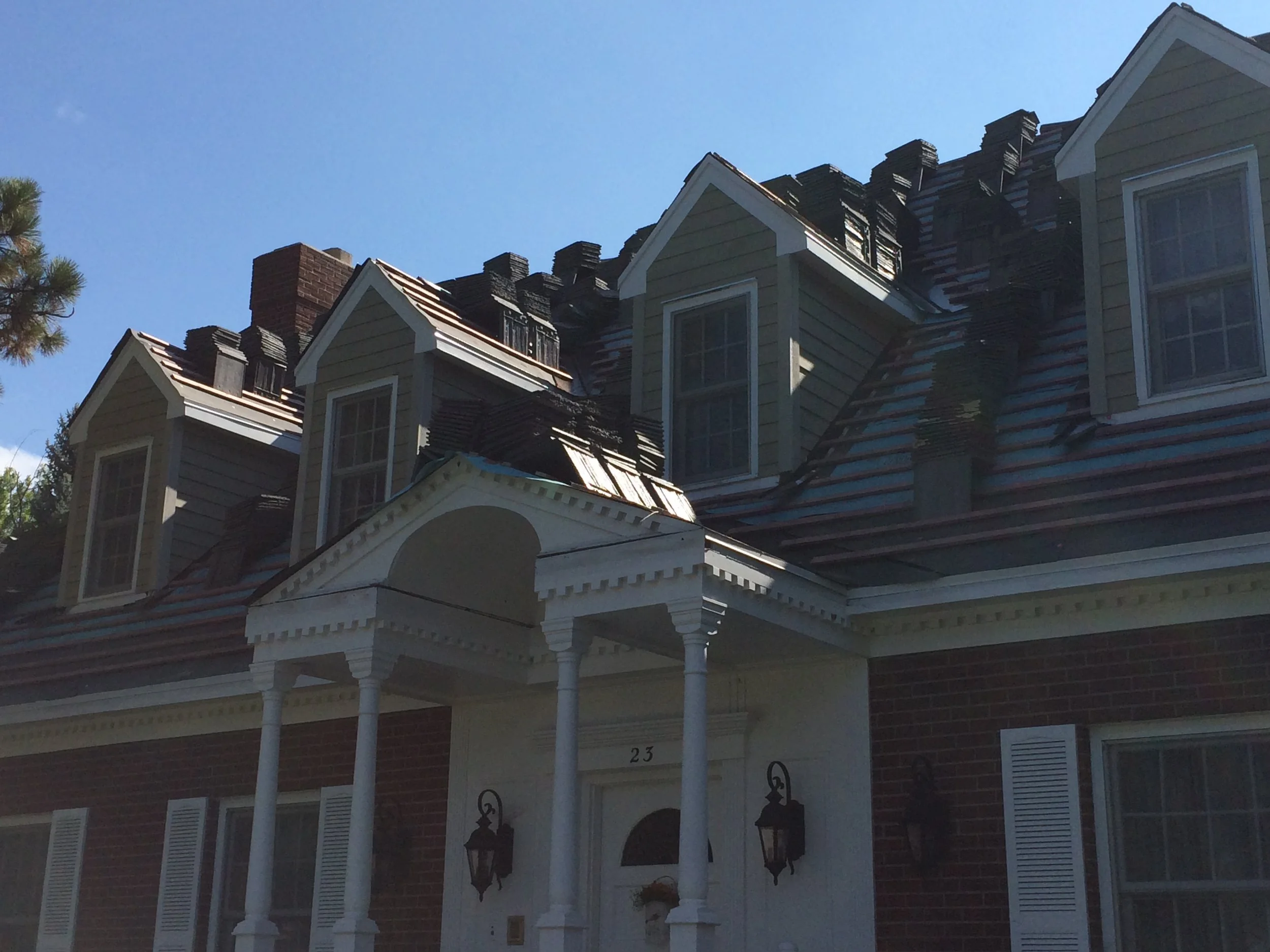 Front view of a house with multiple dormer windows, brick and siding exterior, and a well-maintained porch with columns and lantern-style lights.