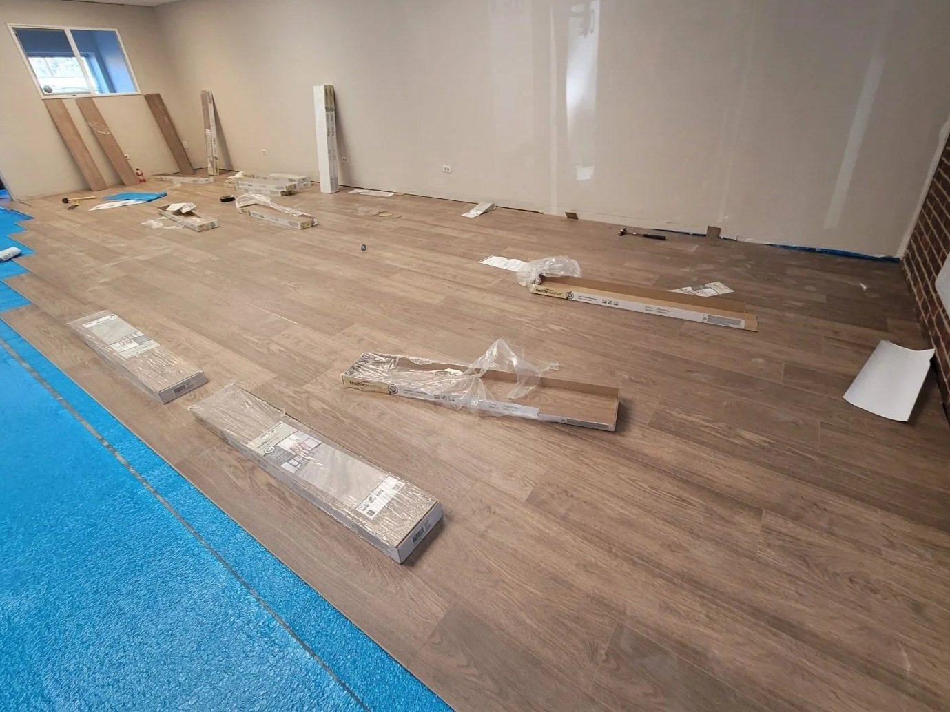 Room with wooden flooring installation in progress, with various tools and flooring packages scattered around.