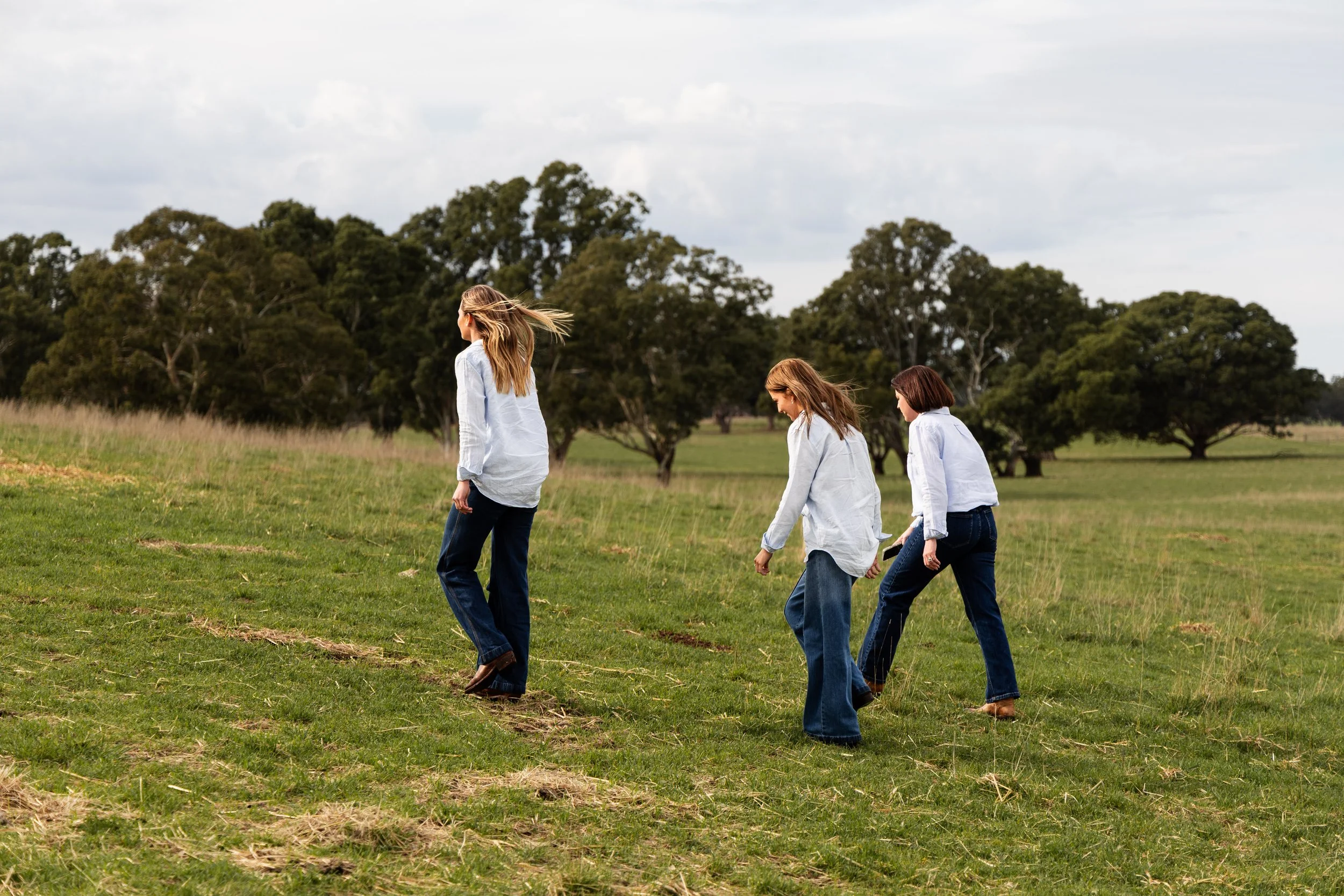 Members of Farm Finance Co Lydia, Alana and Harmony, walking in a line across a grassy field with trees in the background.