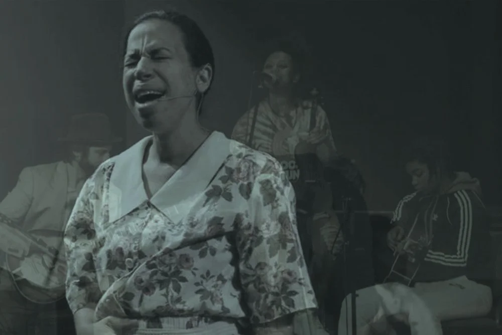 A woman singing passionately during a musical performance with three musicians playing guitars in the background.