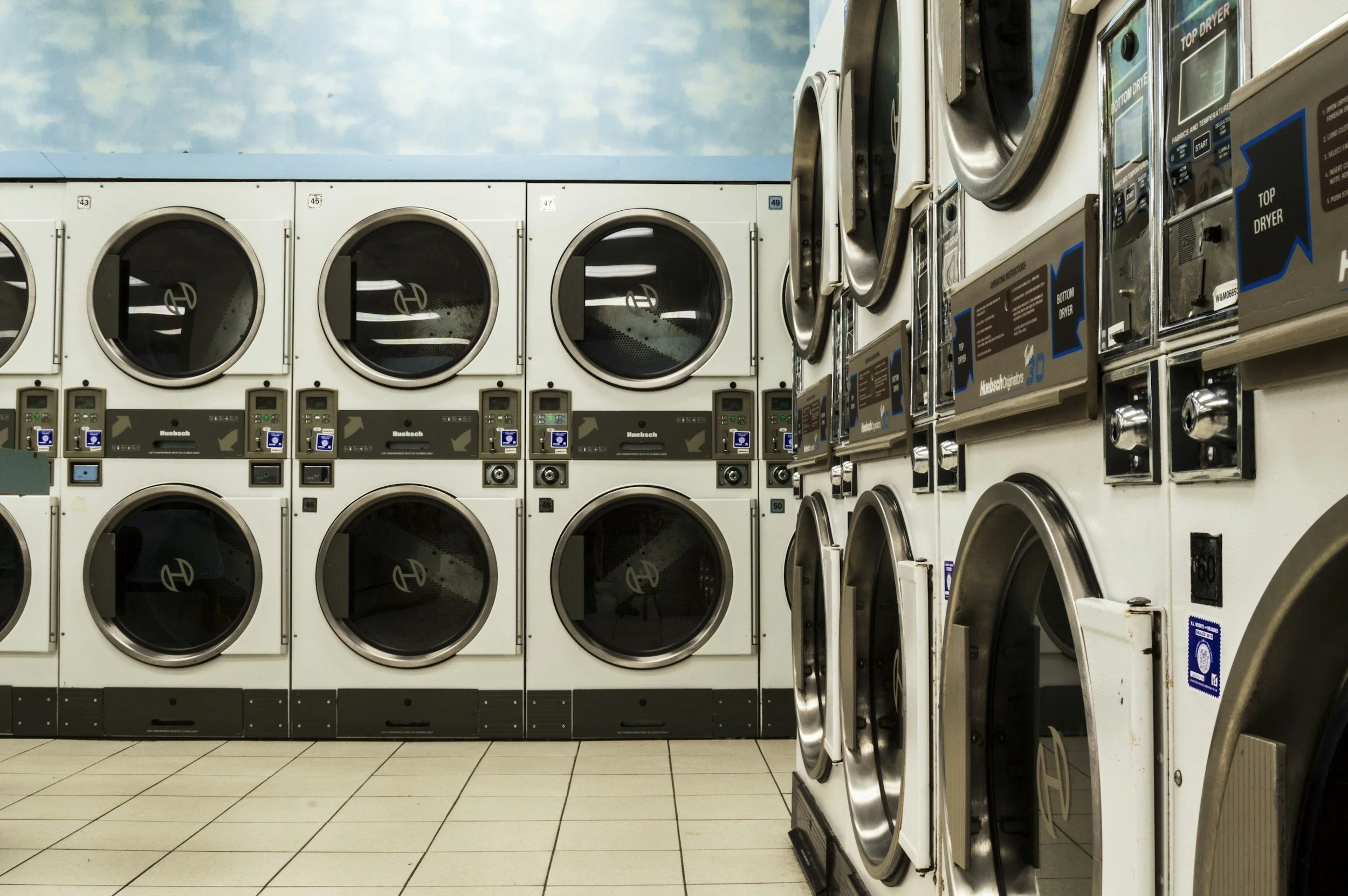 A row of front-loading washing machines and dryers in a laundromat.