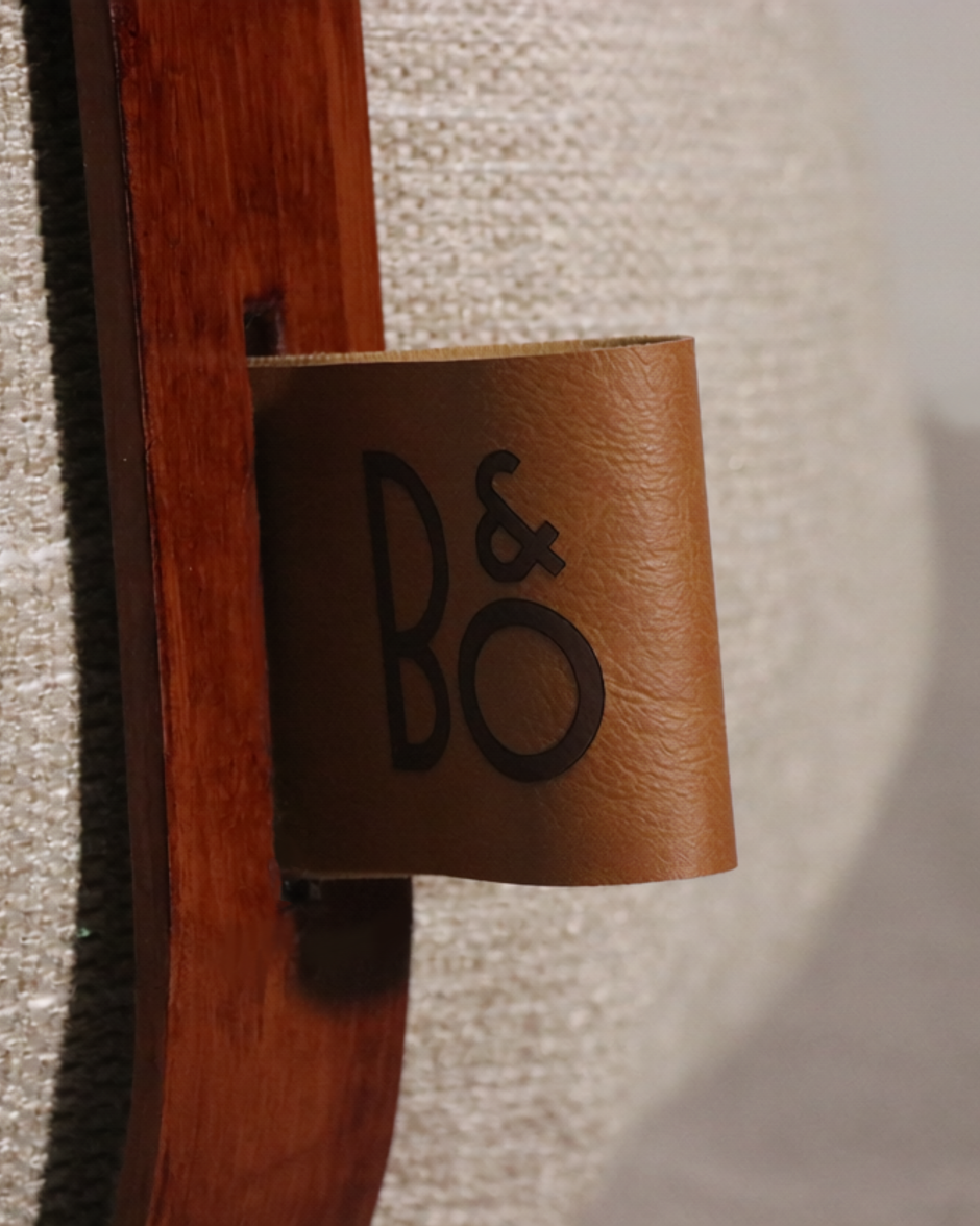 Close-up of a leather tag with 'B&O' logo attached to a wooden surface.
