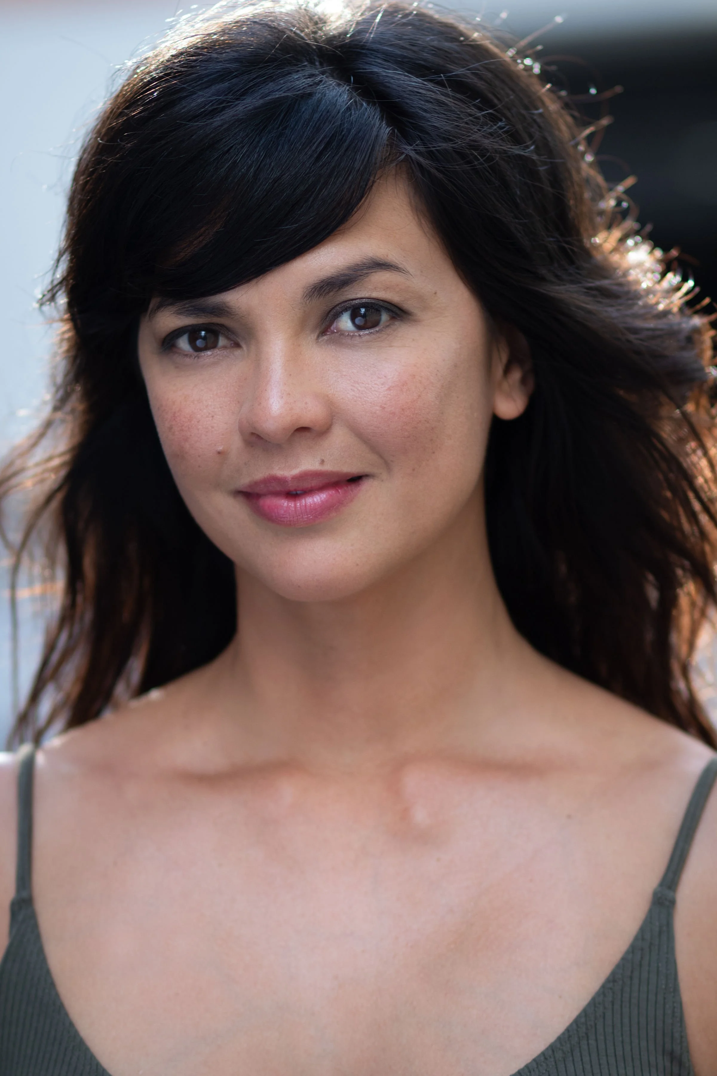 Close-up of woman with dark brown hair, wearing a gray tank top, smiling softly, with a blurred neutral background.