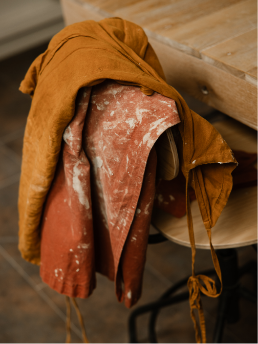 Vêtements suspendus, dont une veste en cuir marron et un vêtement en tissu rose sale, accrochés à une chaise.