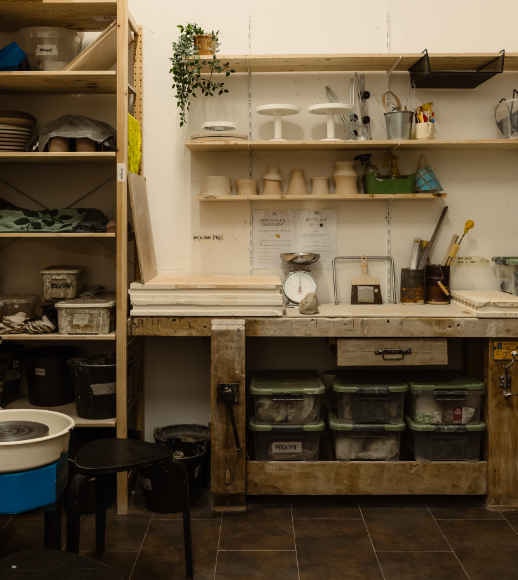 Atelier avec étagères et rangement pour aménagements artistiques ou artisanaux, comprenant céramiques, outils, boîtes de stockage, et plantes vertes.