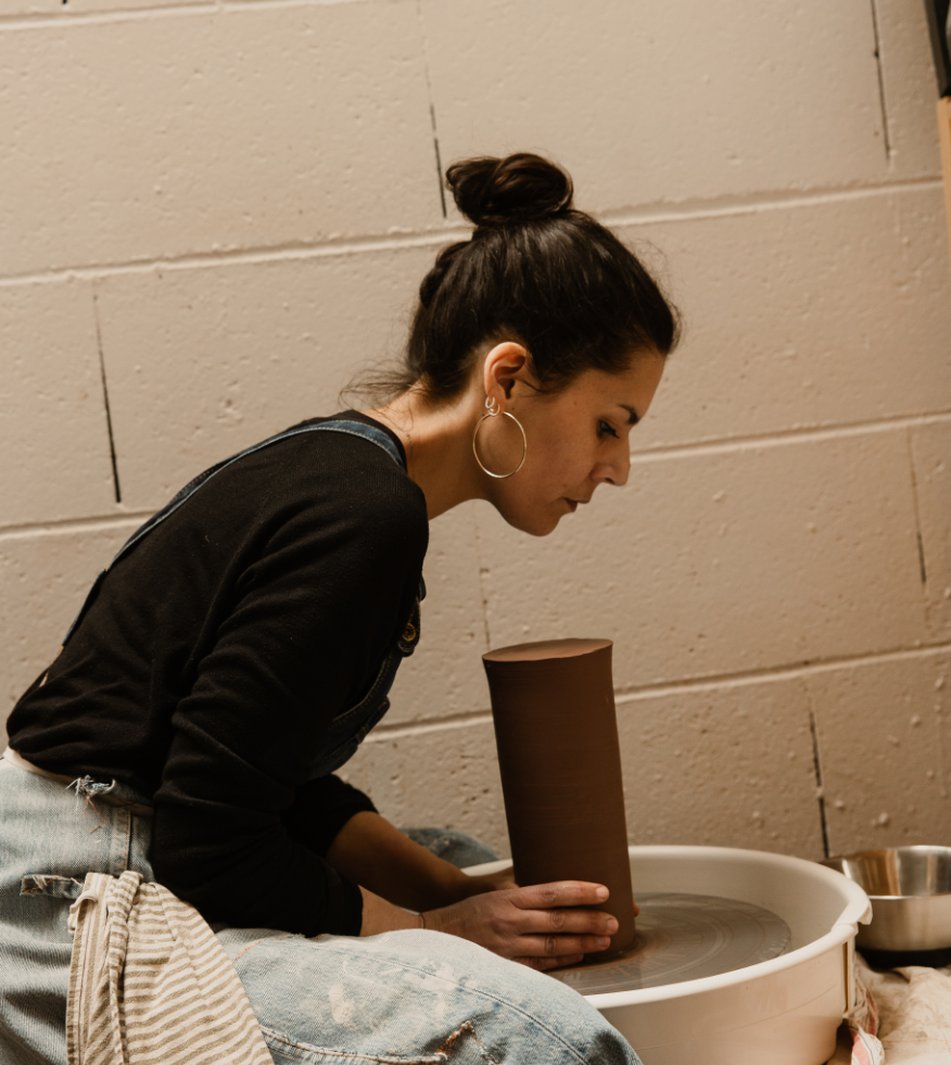 Une femme assise en train de faire de la poterie sur un tour de potier.