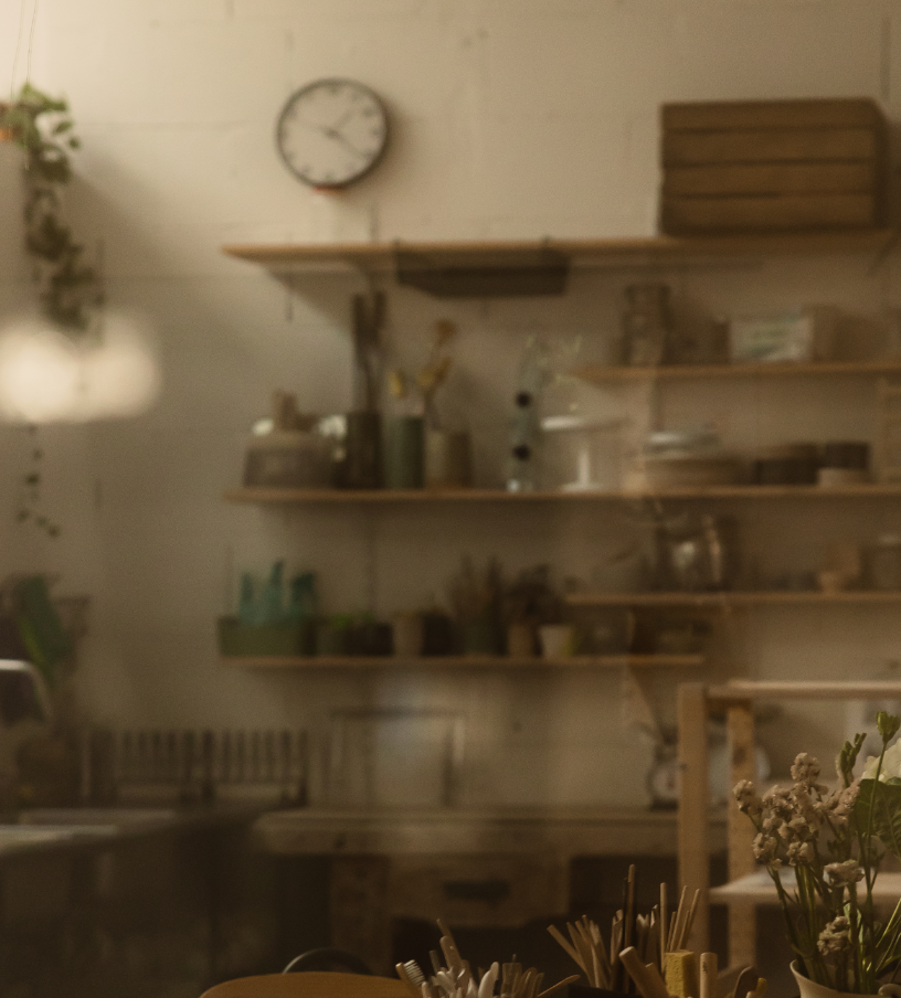 Intérieur d'un café ou d'une boutique avec étagères en bois, horloge murale, plantes et divers objets décoratifs.