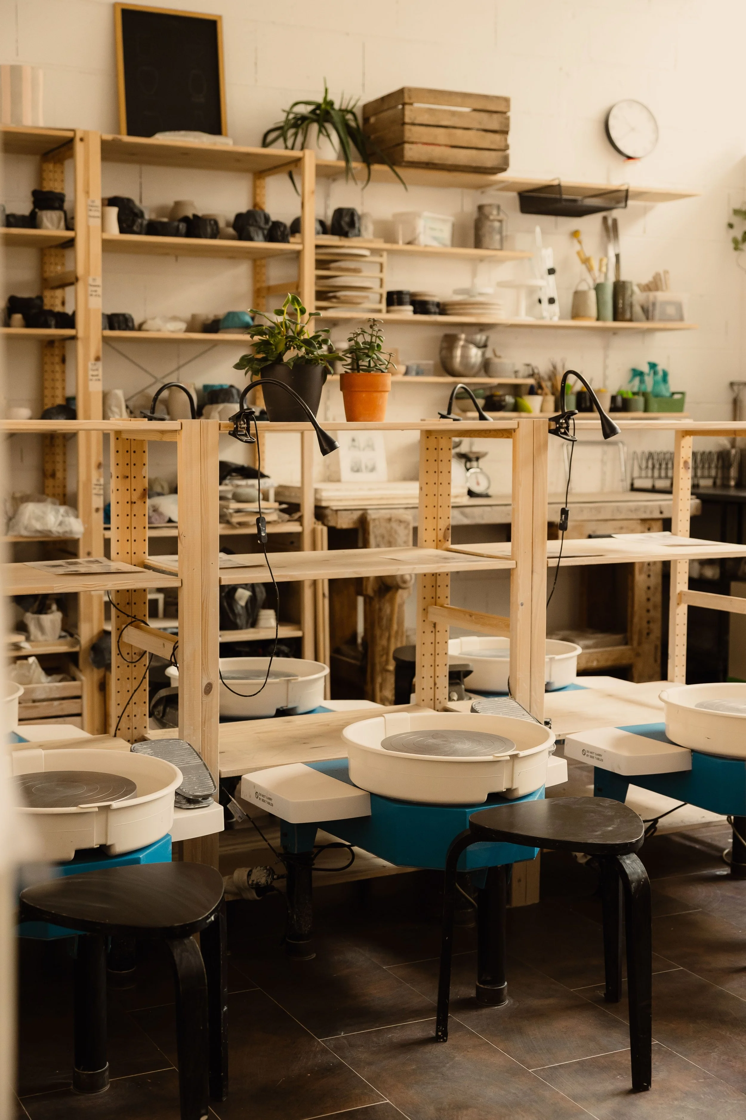 Salle de classe ou atelier avec planches en bois, appareils de poterie et plantes décoratives.