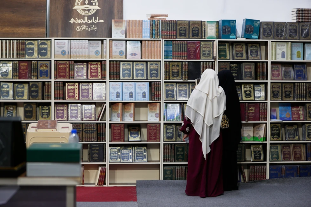 A woman wearing hijab browses large shelves of books.