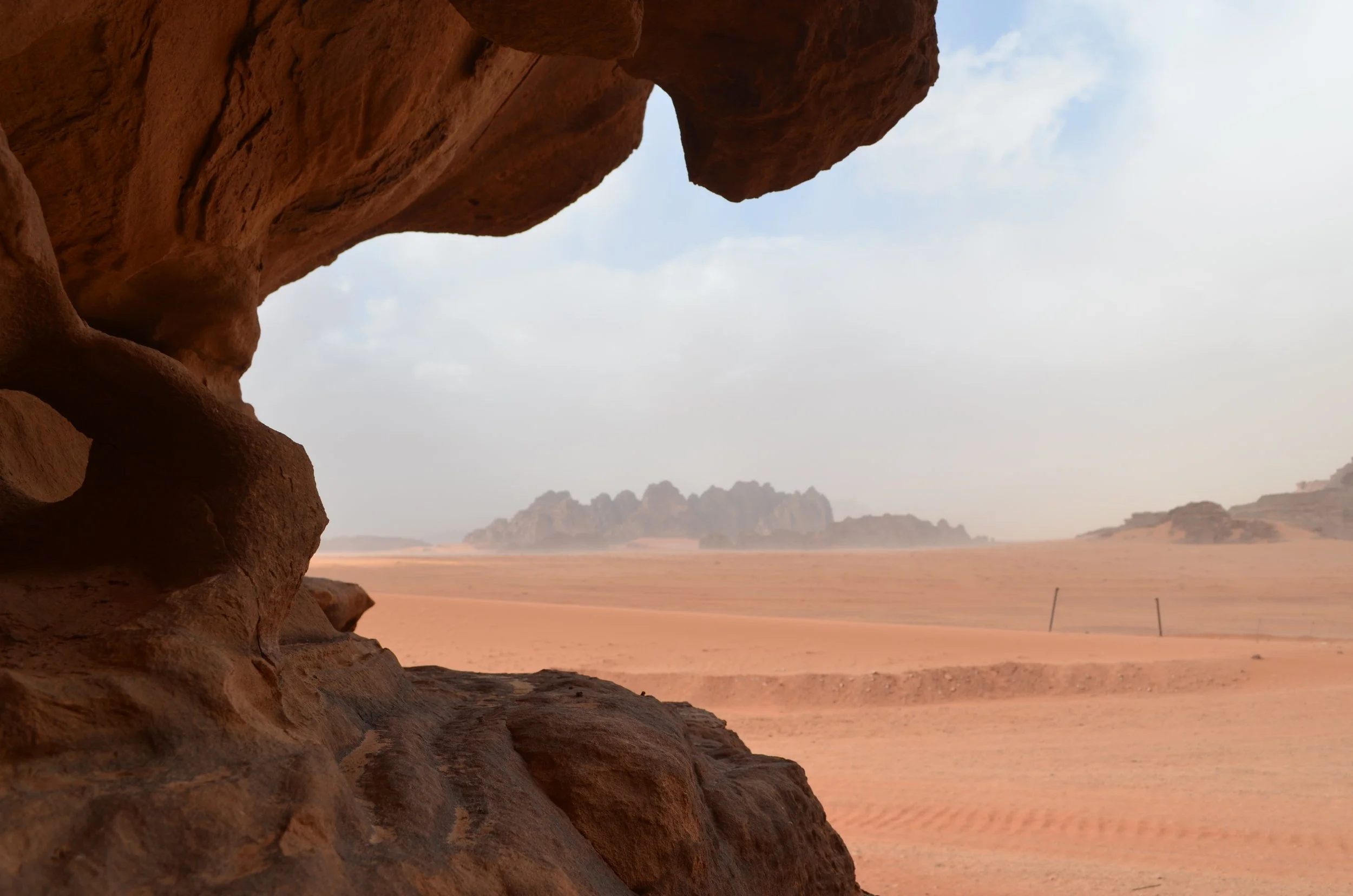 A view of a desert landscape with rocky formations in the distance, taken from inside a cave or rock crevice.