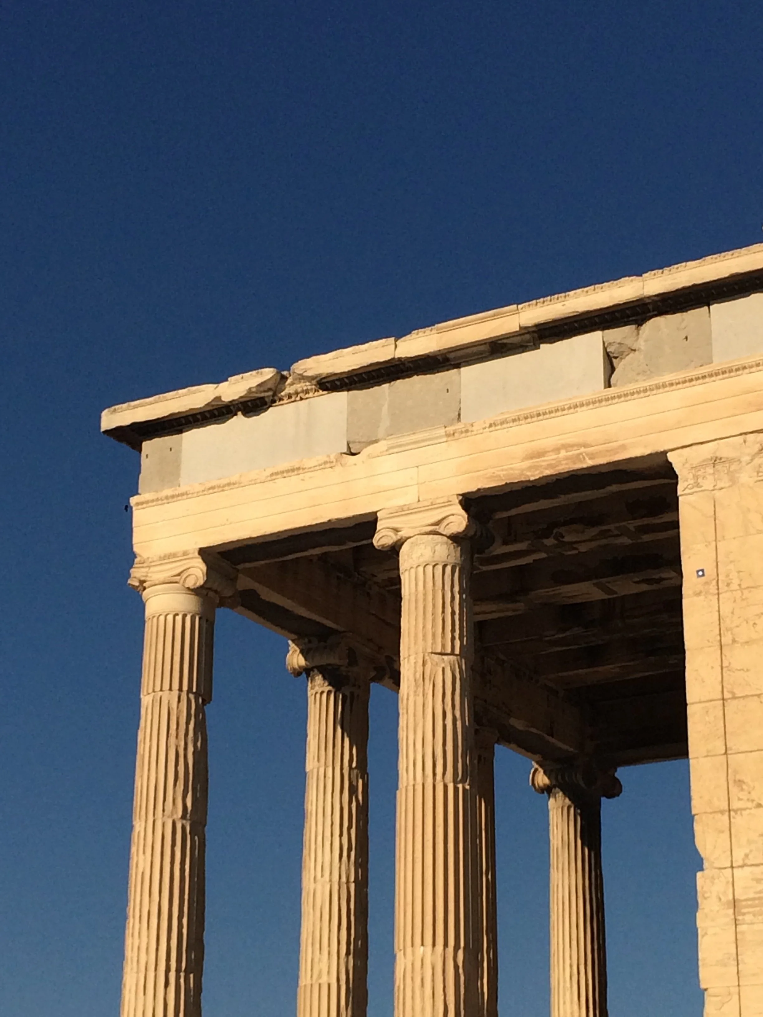 Ancient Greek temple ruins with tall, fluted columns and a partially intact entablature, against a clear blue sky.