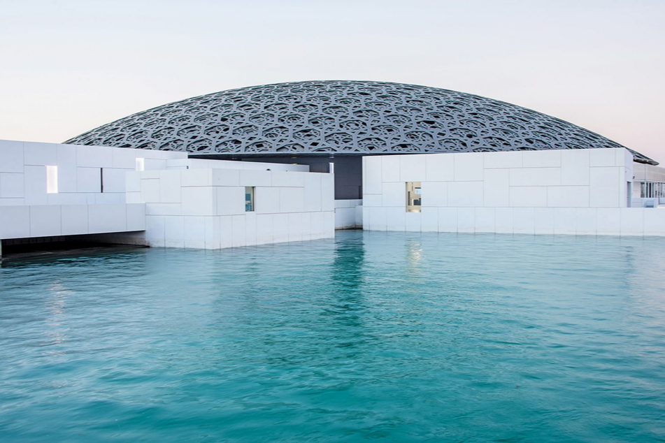 Modern building with a large, decorative, lattice-patterned dome roof next to turquoise water.