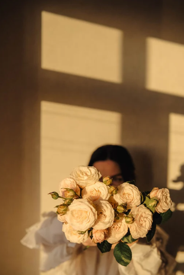 Mujer sosteniendo un ramo de rosas blancas con sombras de ventanas en la pared.