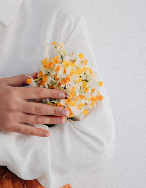 Mano sosteniendo un ramo de flores blancas y amarillas sobre una tela blanca