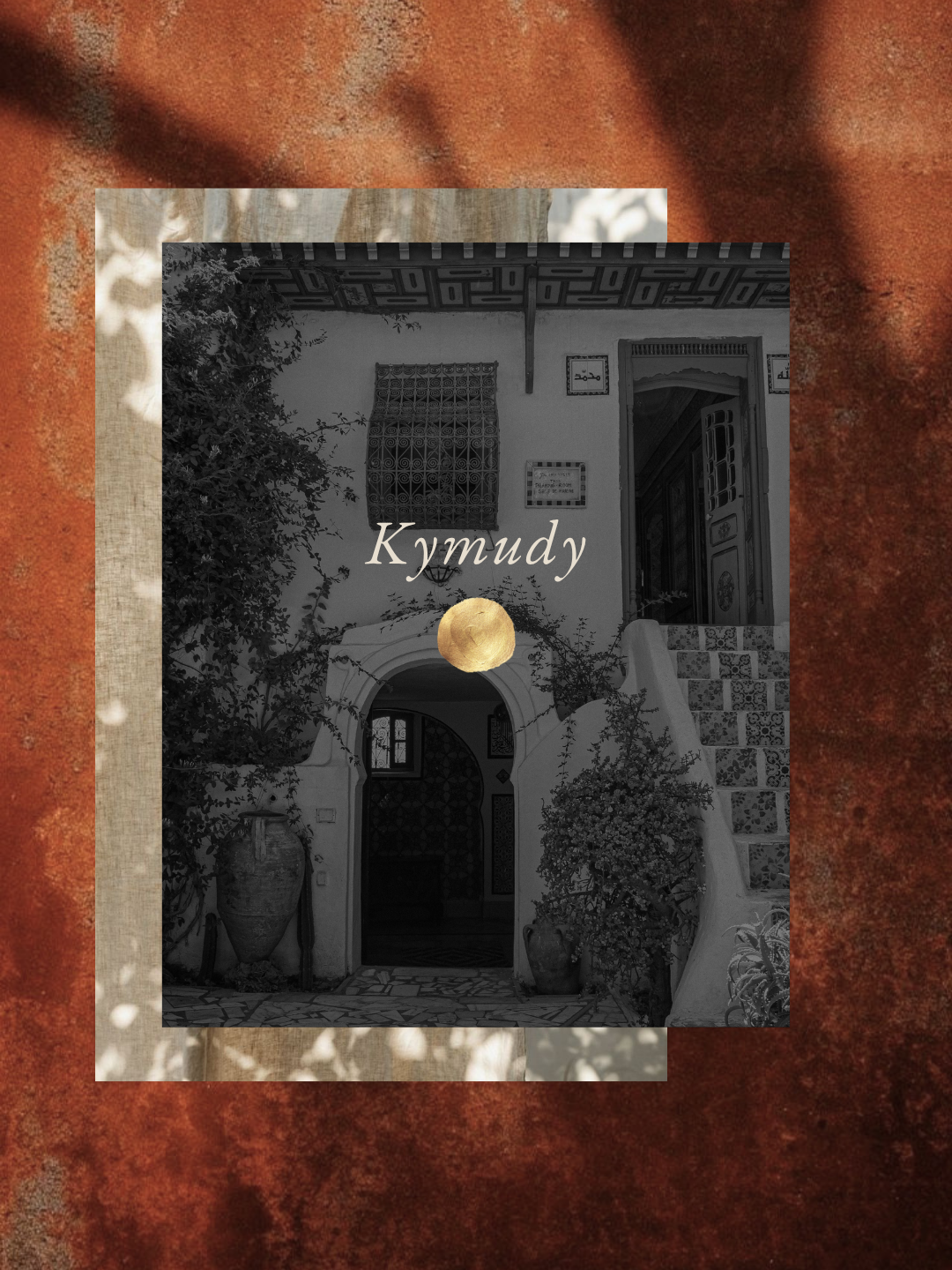 Couverture de livre avec une photo en noir et blanc d'une maison marocaine avec plantes et escaliers, le titre 'Kymudy' en lettres cursives et un cercle doré au centre.