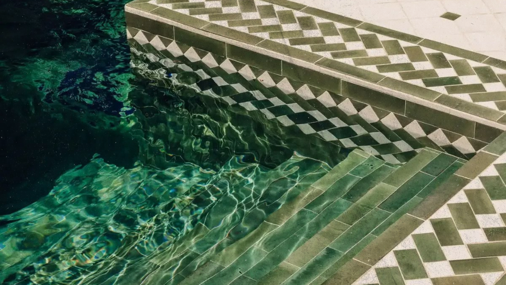 Escalier de piscine en mosaïque verte avec motif géométrique, reflet dans l'eau de la piscine. Photographe hôtel et espace bien-être.