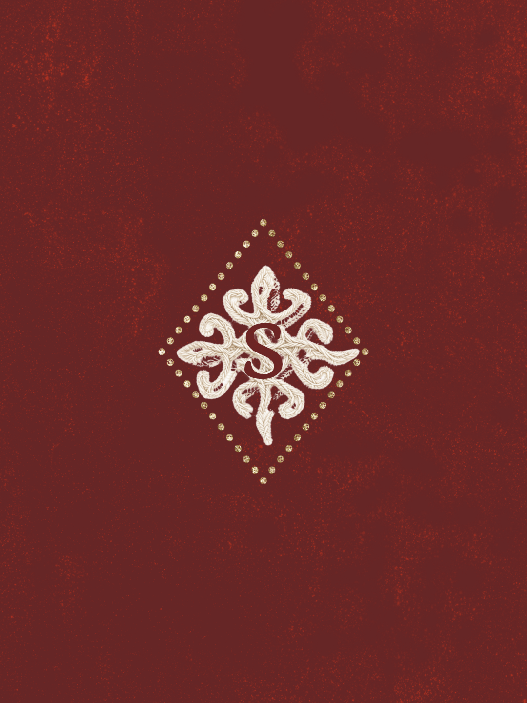 Détail d'une broderie blanche avec un 'S' central, entourée de motifs floraux, sur un fond rouge. Logo chambre d'hôtes.