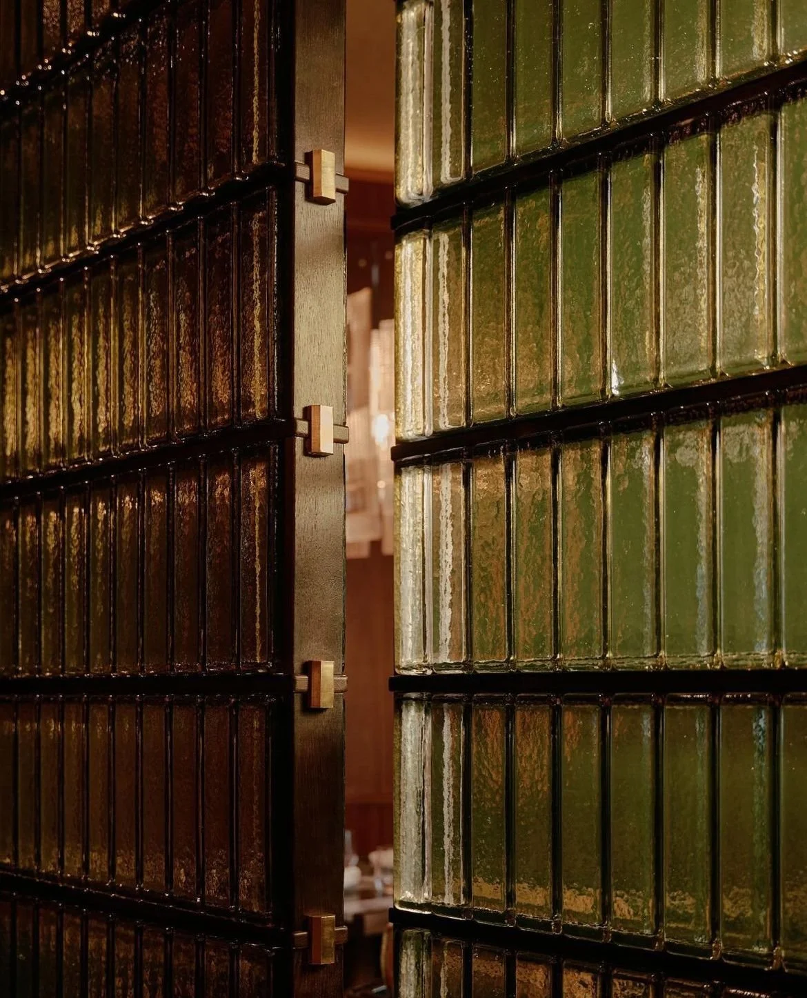 Une cloison en carreaux de verre vert foncé avec une ouverture, laissant entrevoir une pièce intérieure. Détail déco dans une maison d'hôtes en Normandie.