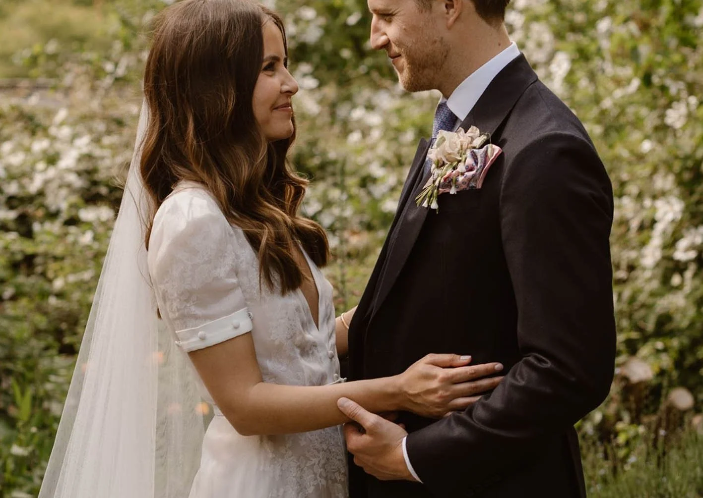 A bride and groom standing face-to-face outdoors during their wedding, holding each other gently and smiling at each other.