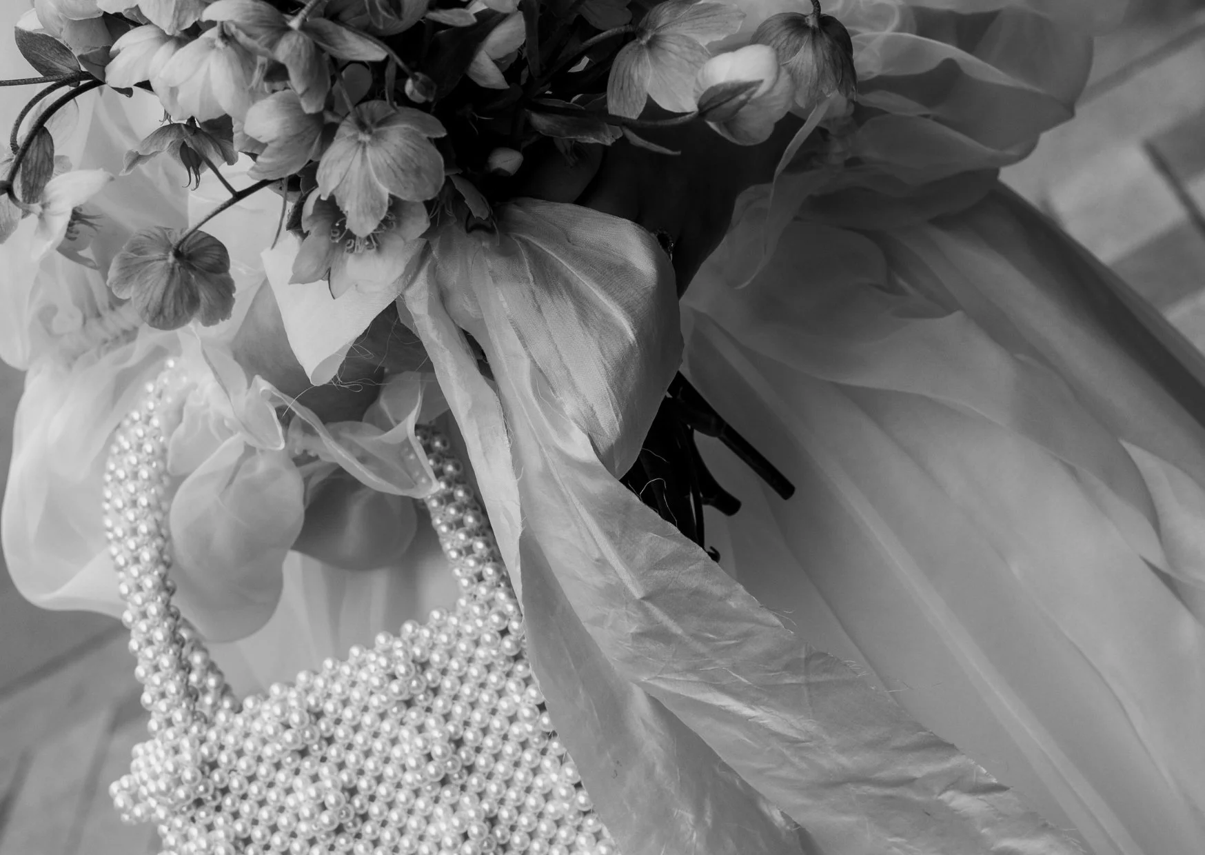 A bouquet of flowers with multiple strands of pearl necklaces draped over it, wrapped in tissue paper.