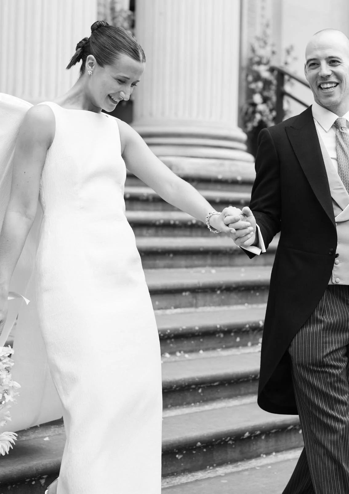 A bride and groom holding hands and smiling on the steps of a building during a wedding.