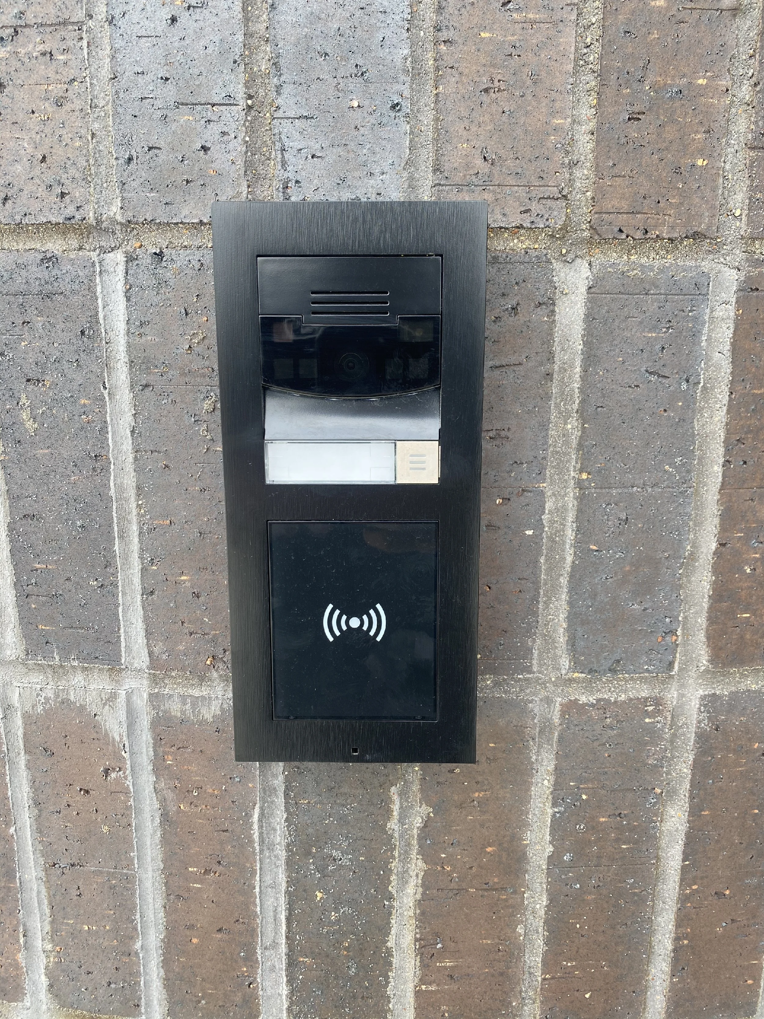Black intercom and access control panel mounted on a brick wall.