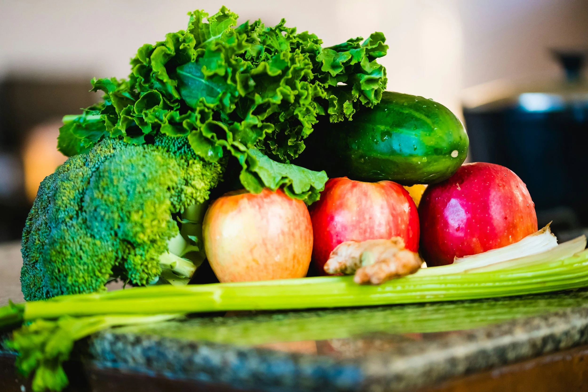 A colorful display of fresh vegetables including broccoli, lettuce, cucumber, apples, and ginger on a green tray.
