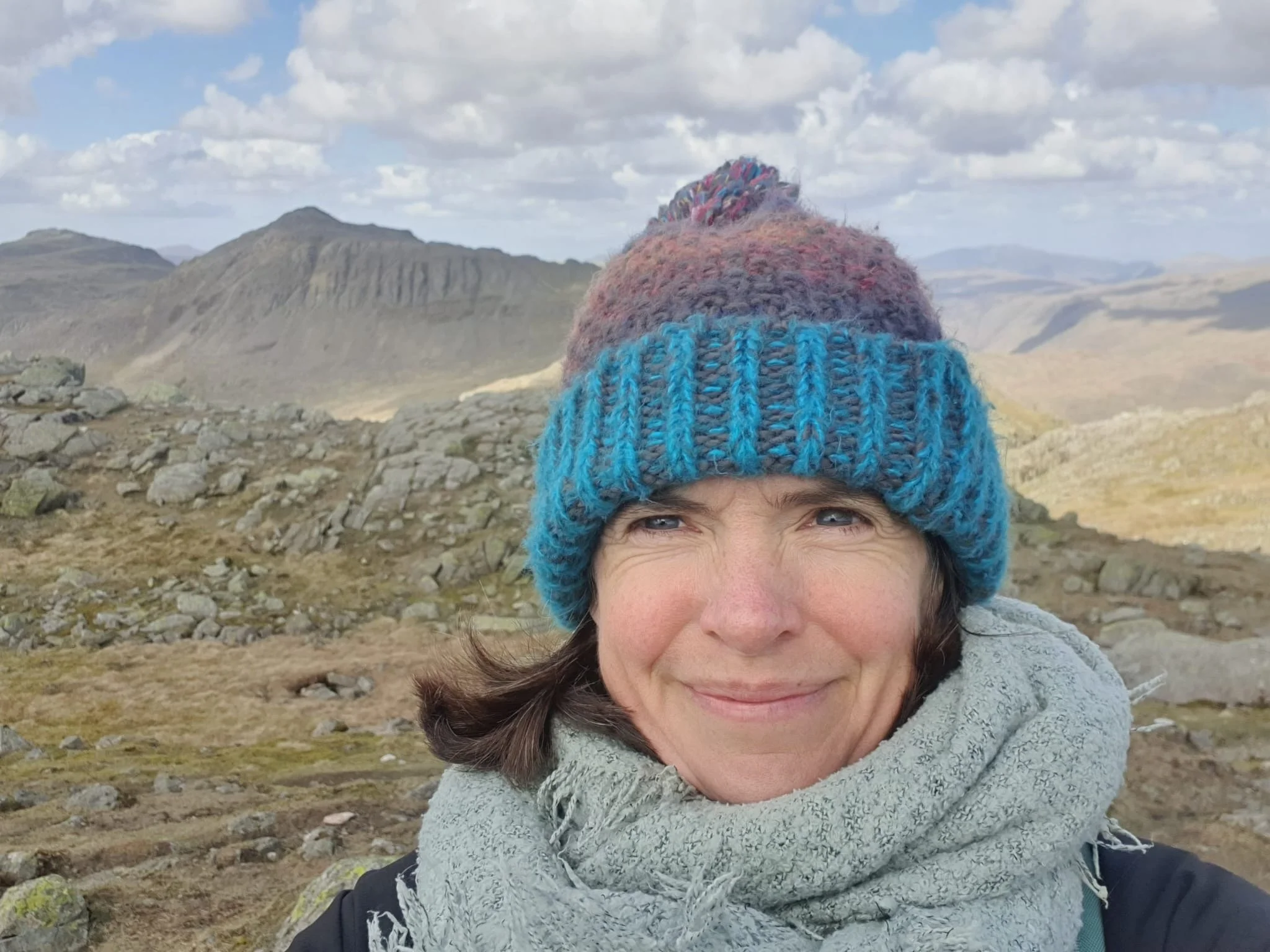 Photo of Hilary wrapped up in a hat and scarf at the top of a mountain.