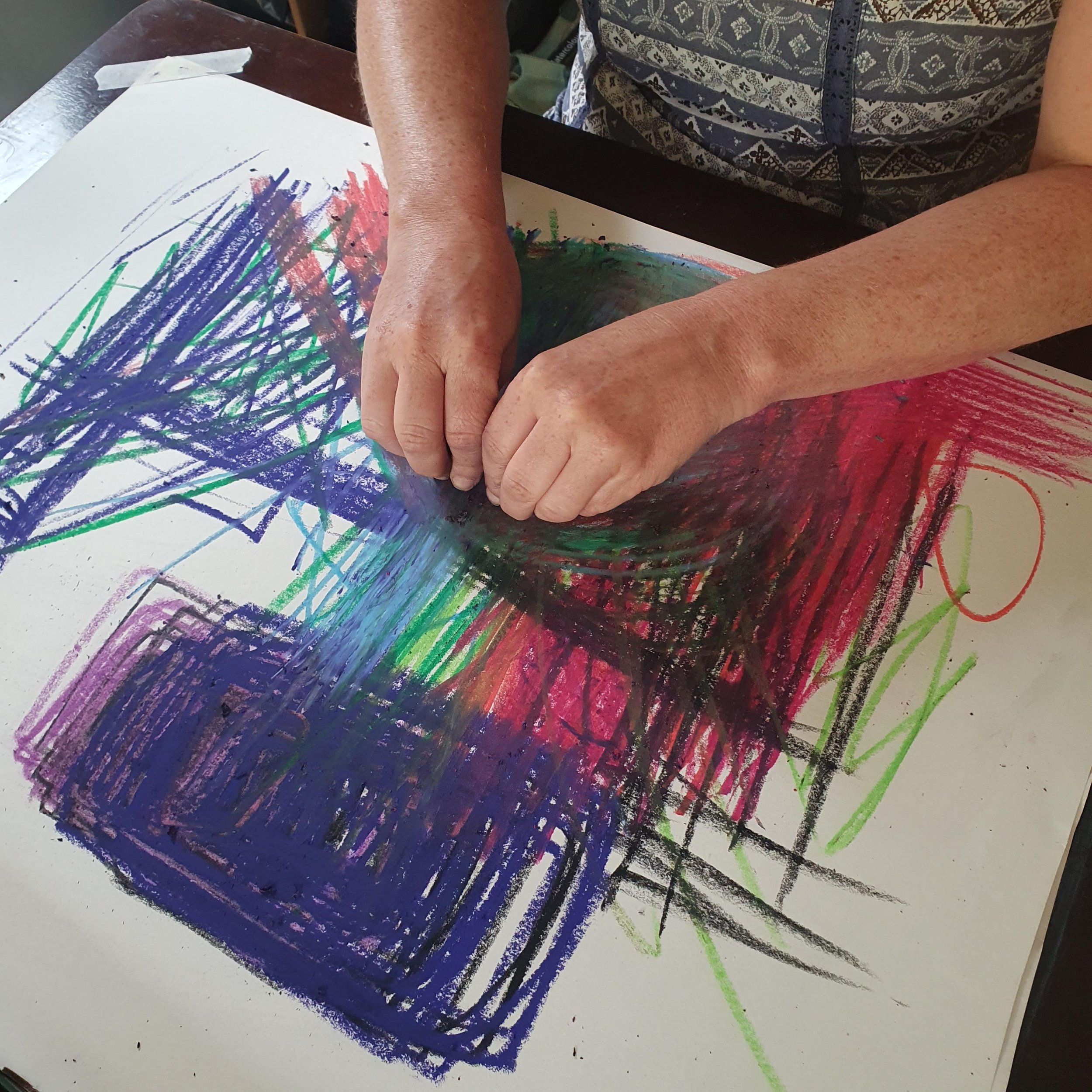 A hands-on moment of Embodied Drawing captured as a client draws vibrant, colorful scribbles using oil pastels using both hands and with eyes closed.