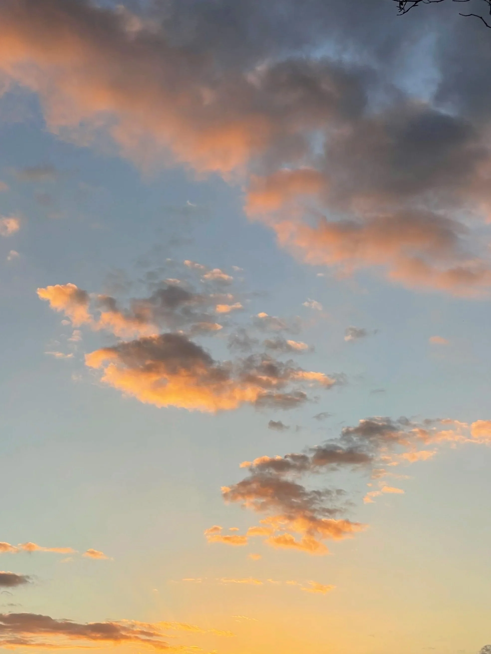 A sky filled with clouds at sunset, displaying shades of orange, pink, and blue.