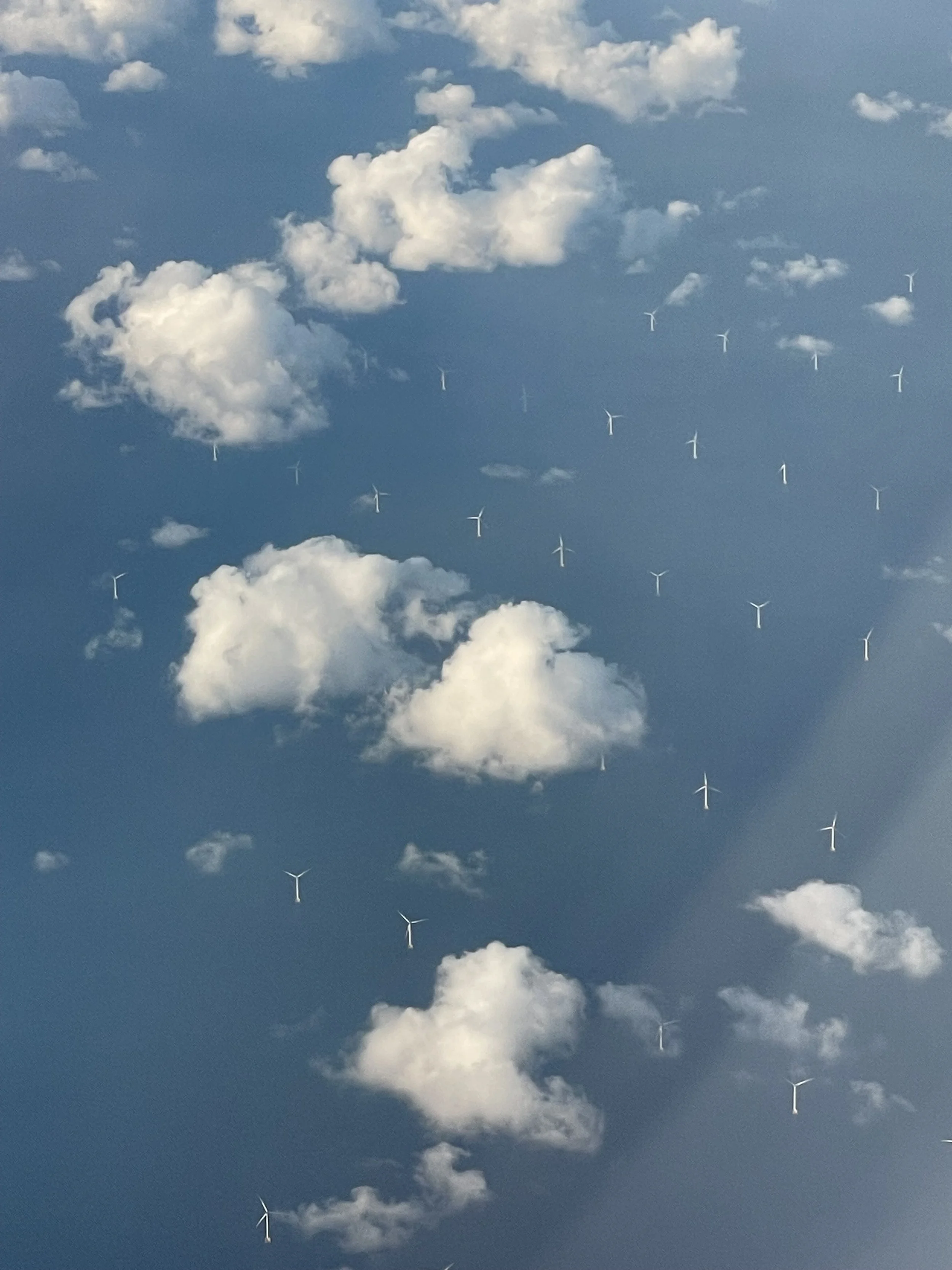 A sky filled with white clouds and multiple wind turbines seen from below.