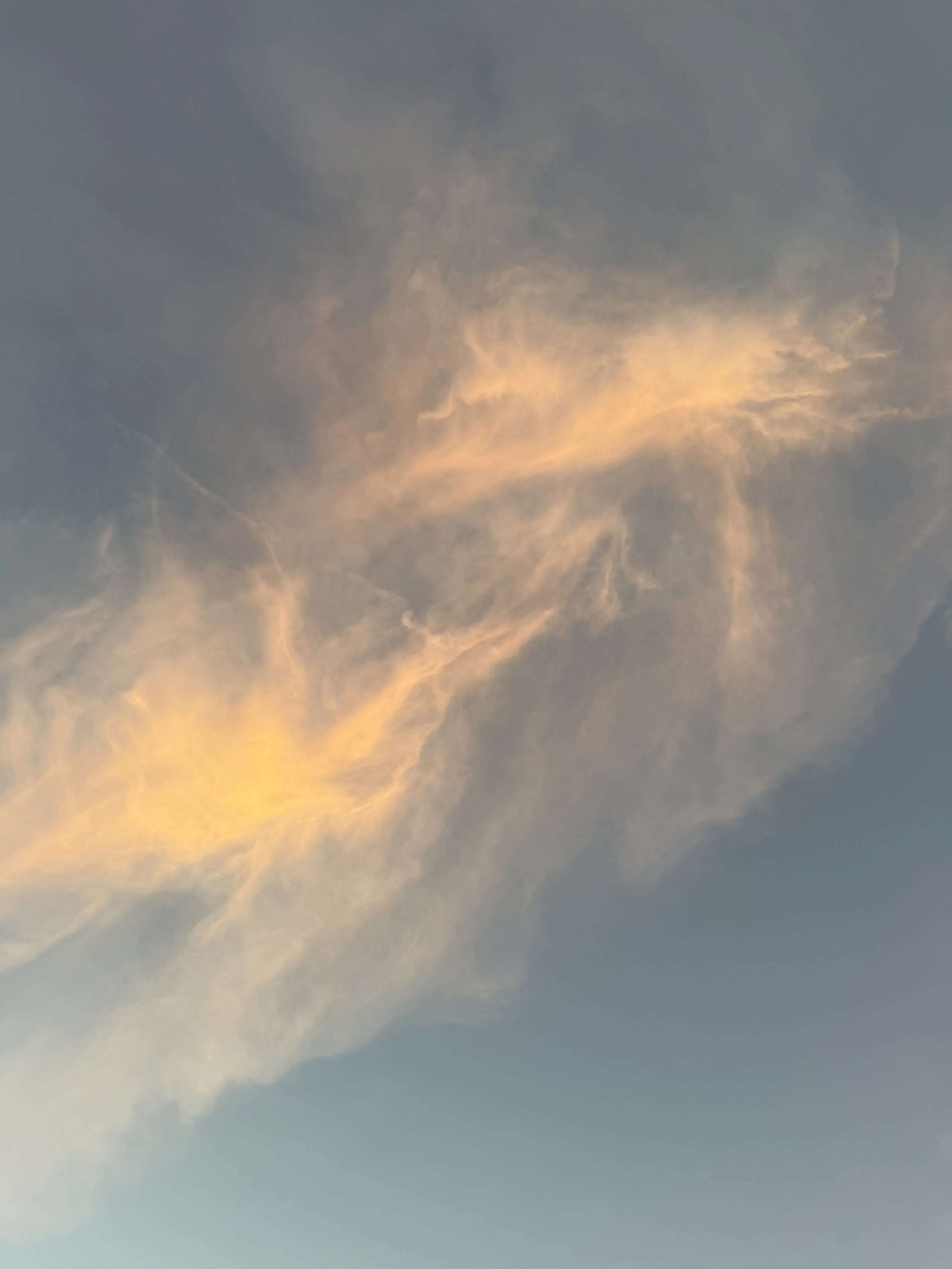 Sky with clouds at sunset, displaying shades of yellow, orange, and blue.