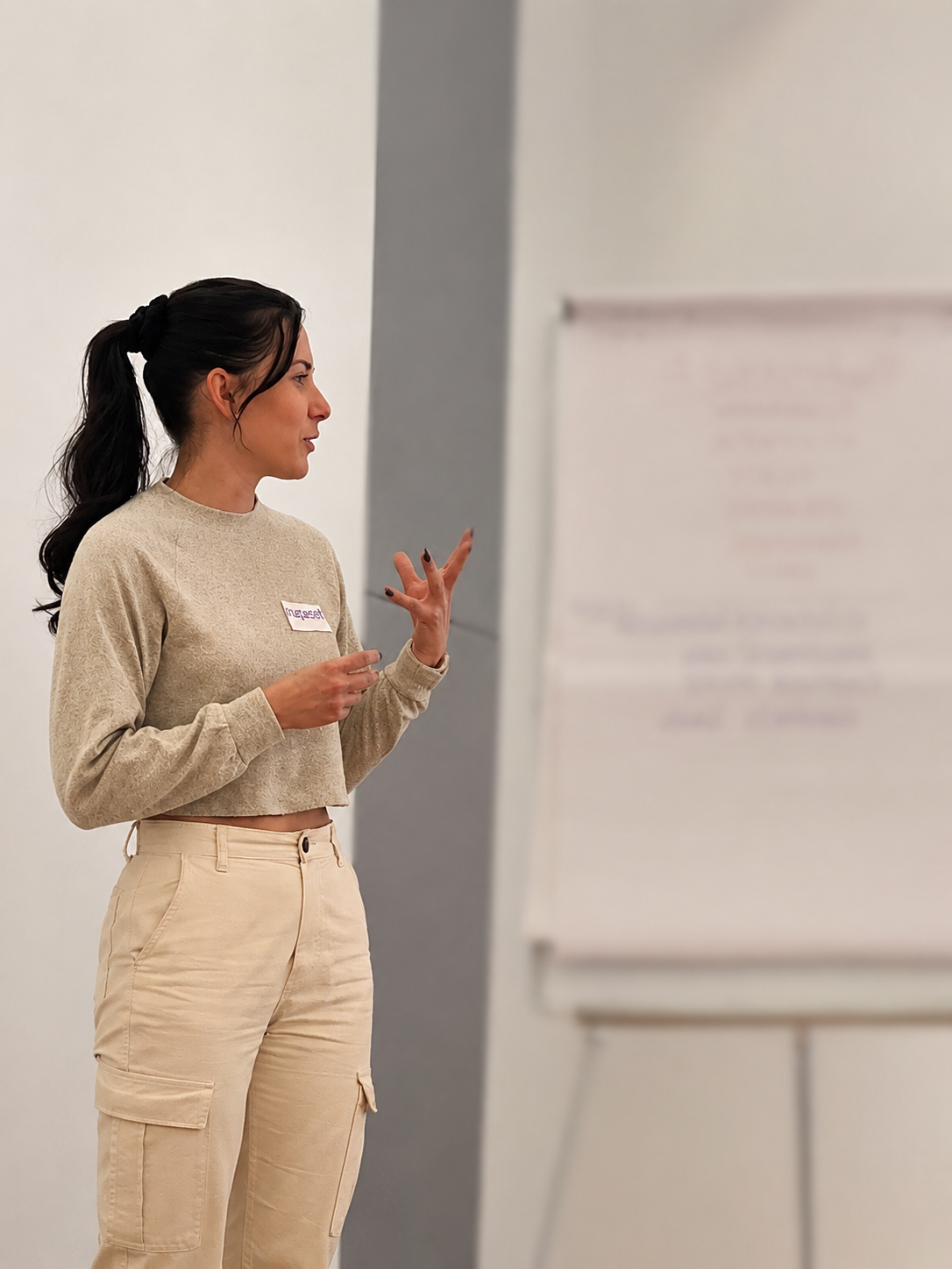 Woman with dark hair tied in a ponytail giving a presentation in front of a whiteboard.