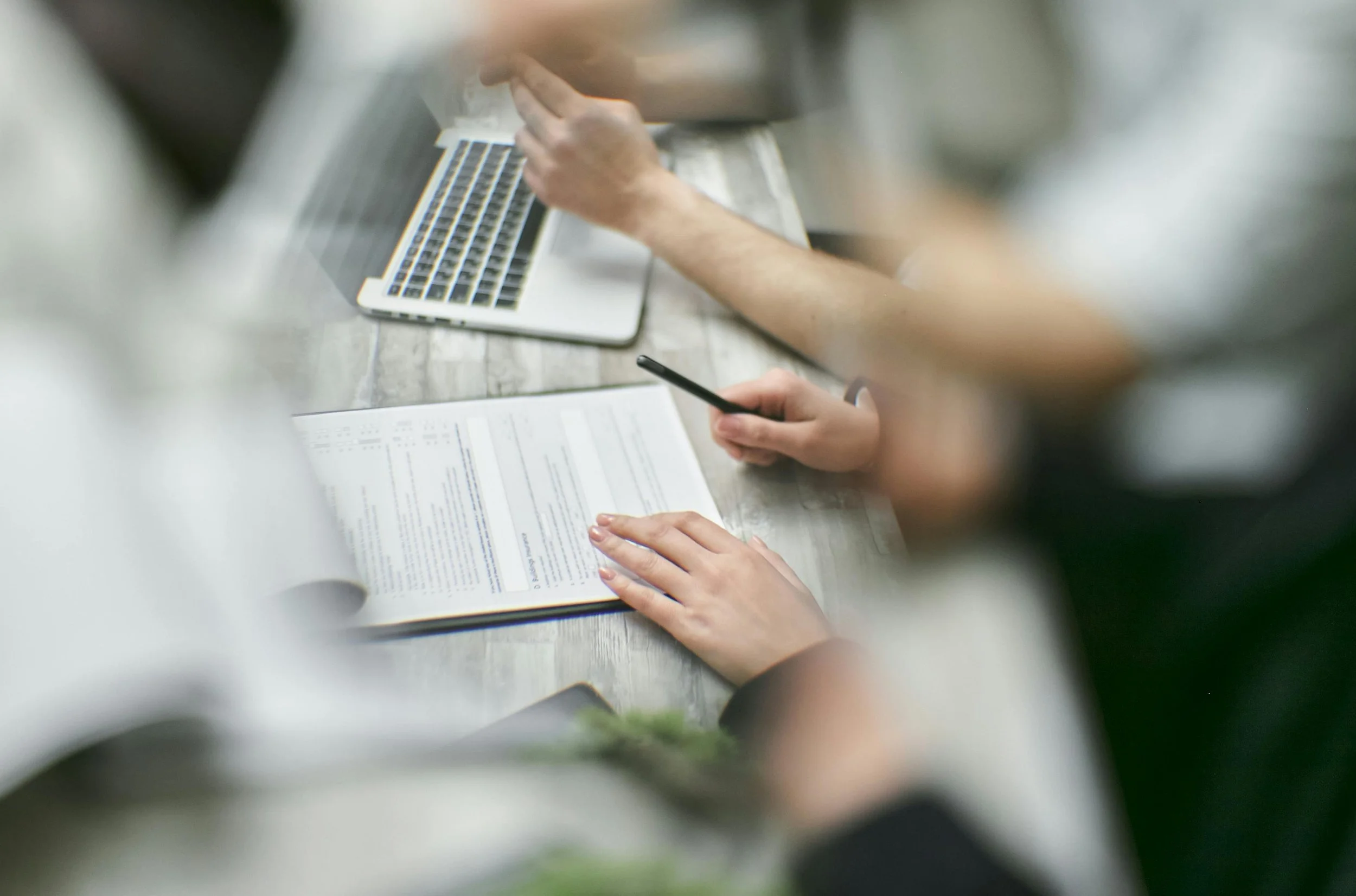 Top-down view of two people working at a table with documents, a smartphone, and a laptop, showing a collaborative work or study session.