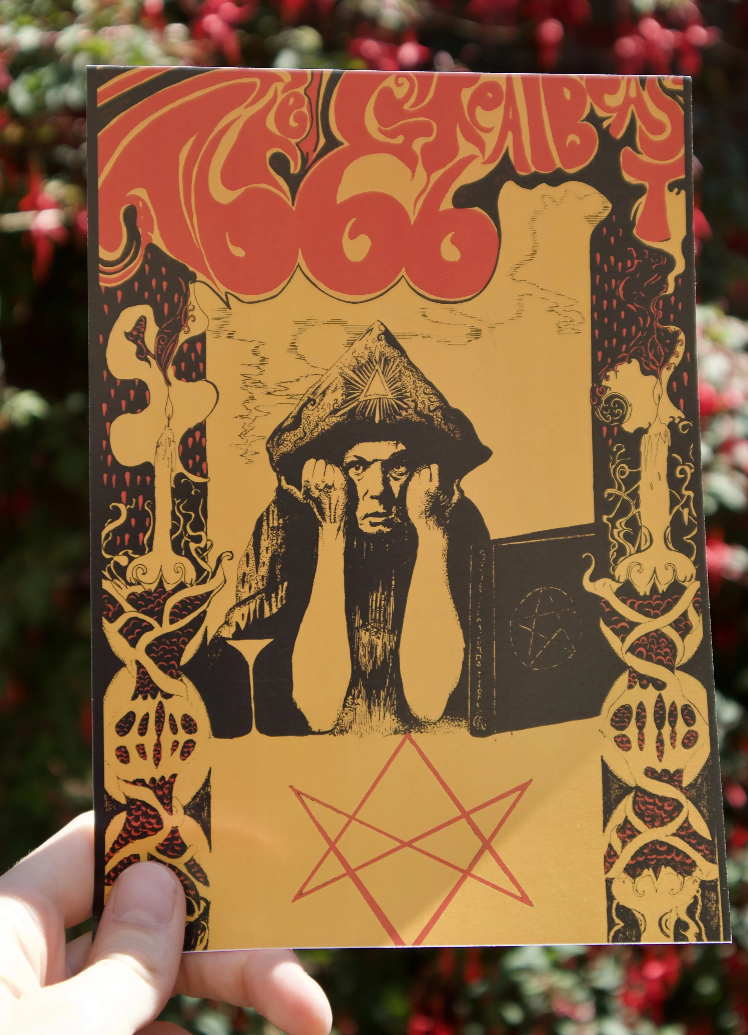 The Great Beast 666 print held against a floral background - Gothic Art Nouveau Portrait of Aleister Crowley with a pentagram illustrated in red and gold ink.