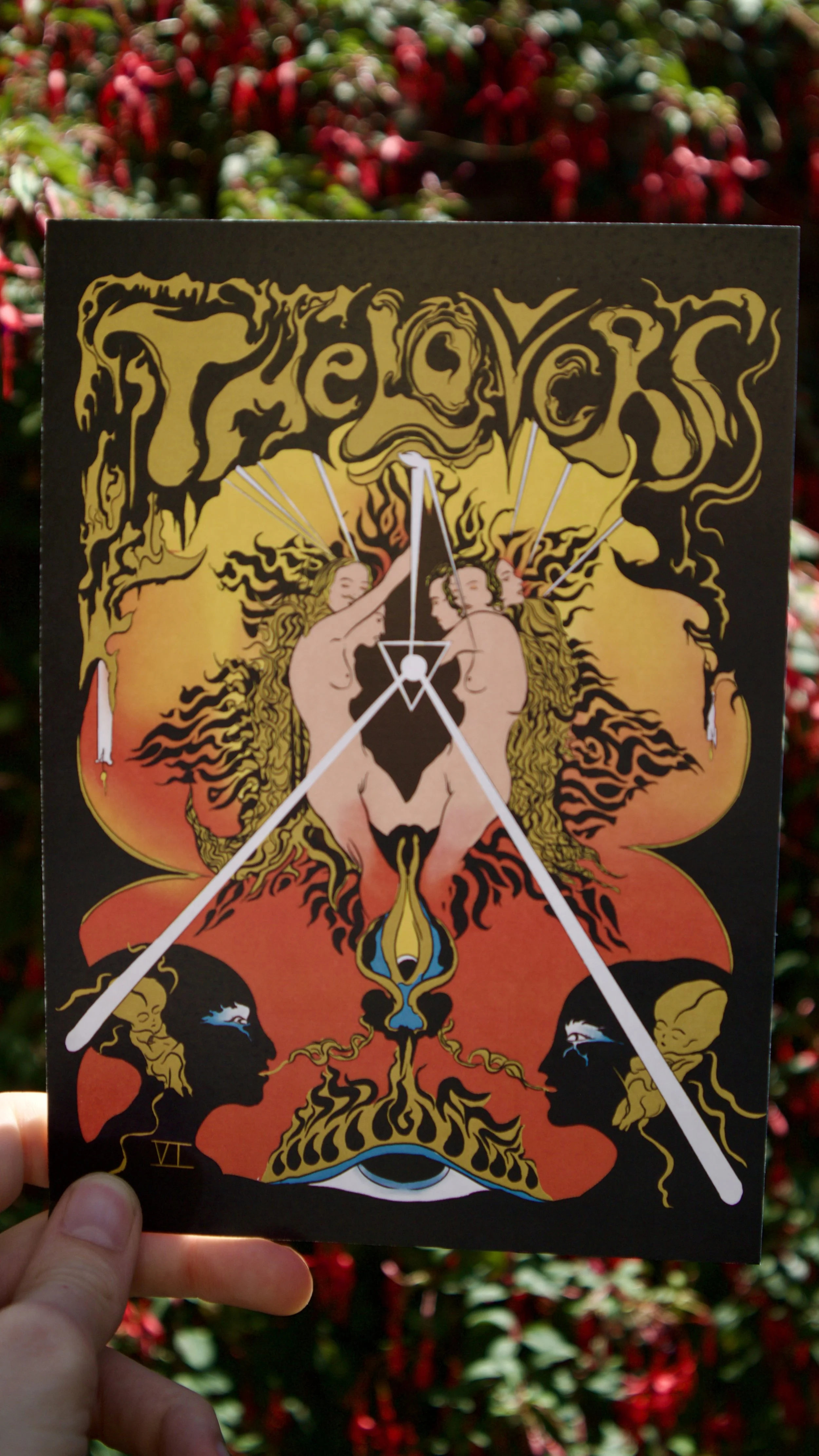 The Lovers tarot card print held against a floral background - a red and gold psychedelic interpretation of the lovers tarot card inspired by 60s psychedelia