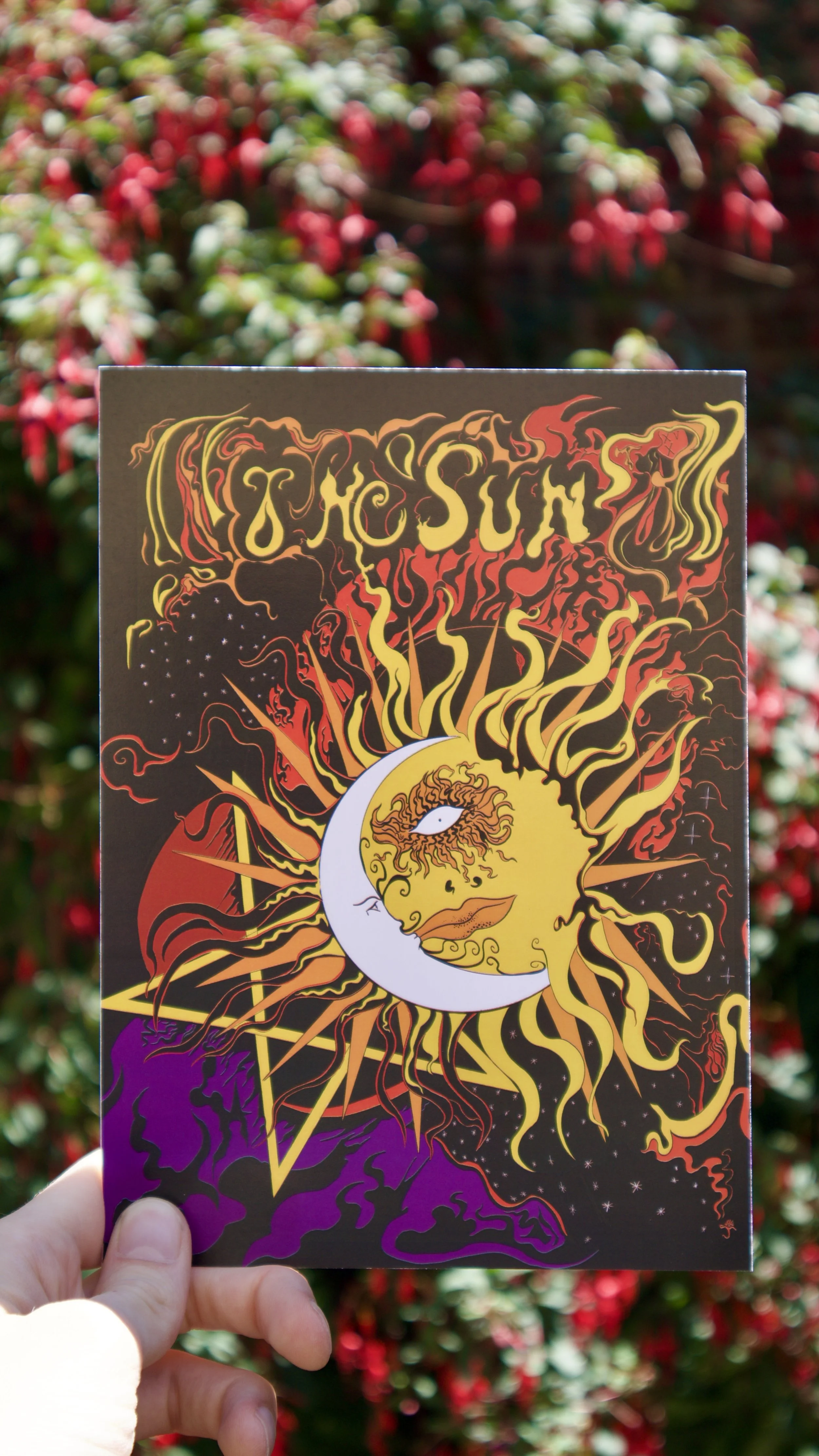 The Sun Tarot print held against a floral backdrop - a colourful psychedelic interpretation of the sun tarot card.