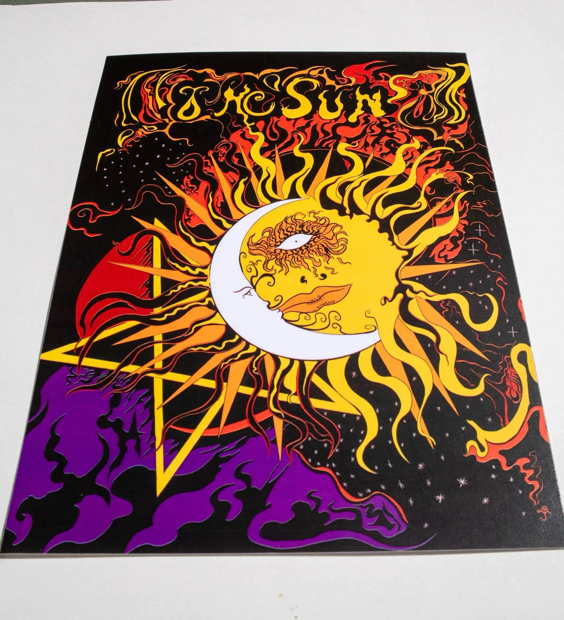 Angled photo of a print featuring a psychedelic image of The Sun tarot card.