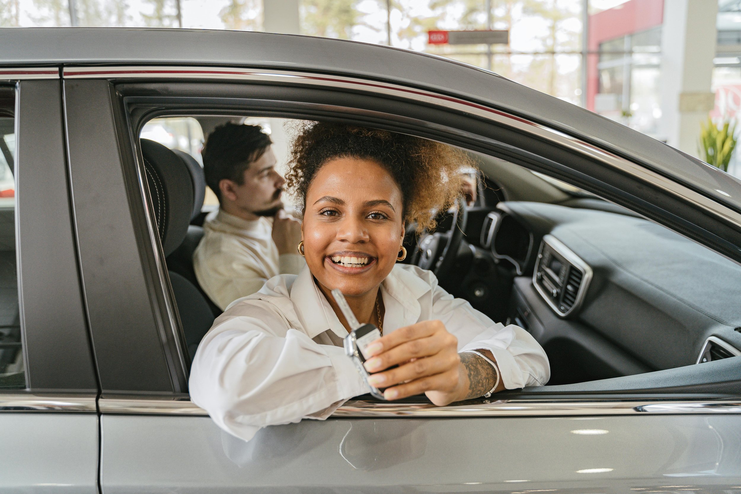 Smiling woman holding a car key while leaning out of a vehicle window.