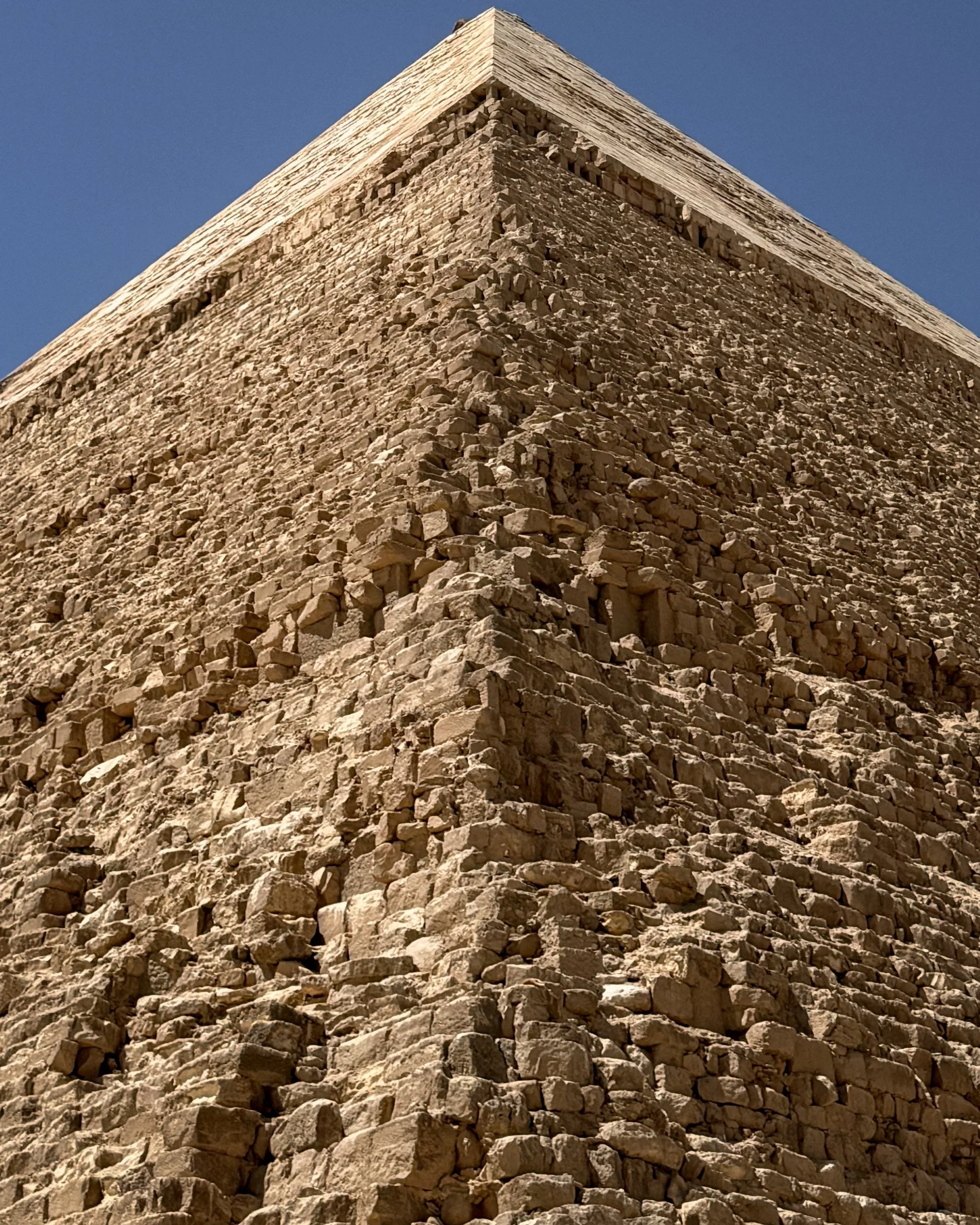 Close-up view of the corner of an ancient stone pyramid with a clear blue sky in the background.
