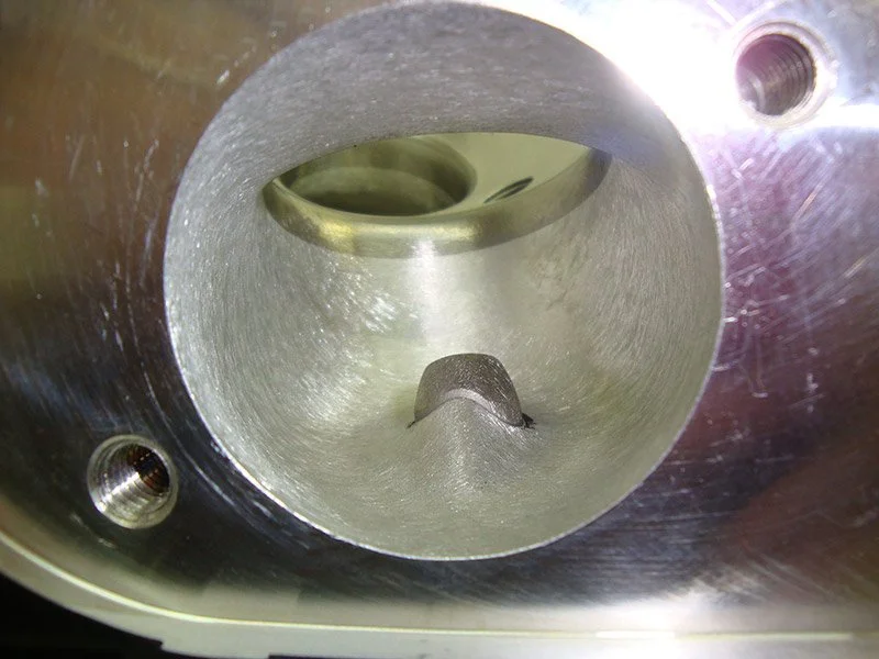 Close-up of a metallic engine cylinder bore with visible threading and a piston inside.