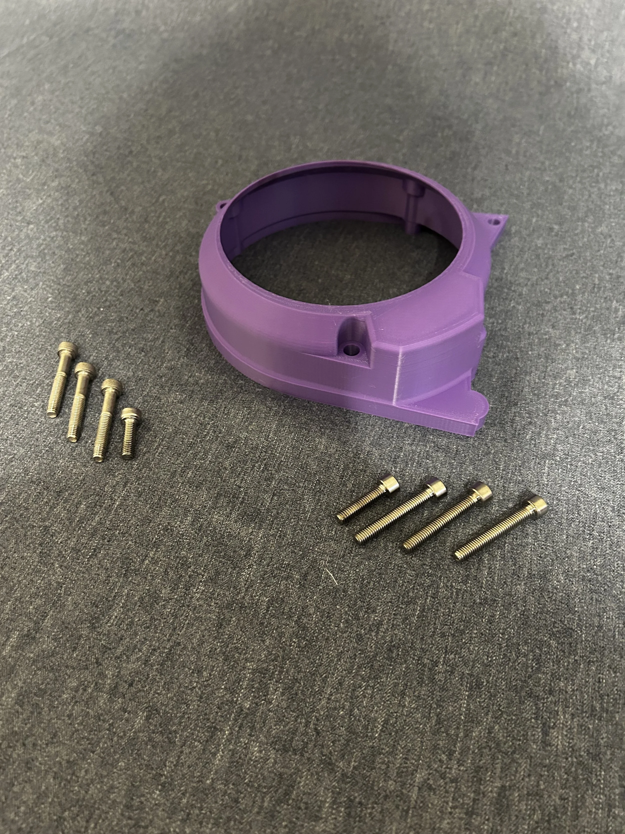 A purple plastic ring with five metal screws on a gray fabric surface.