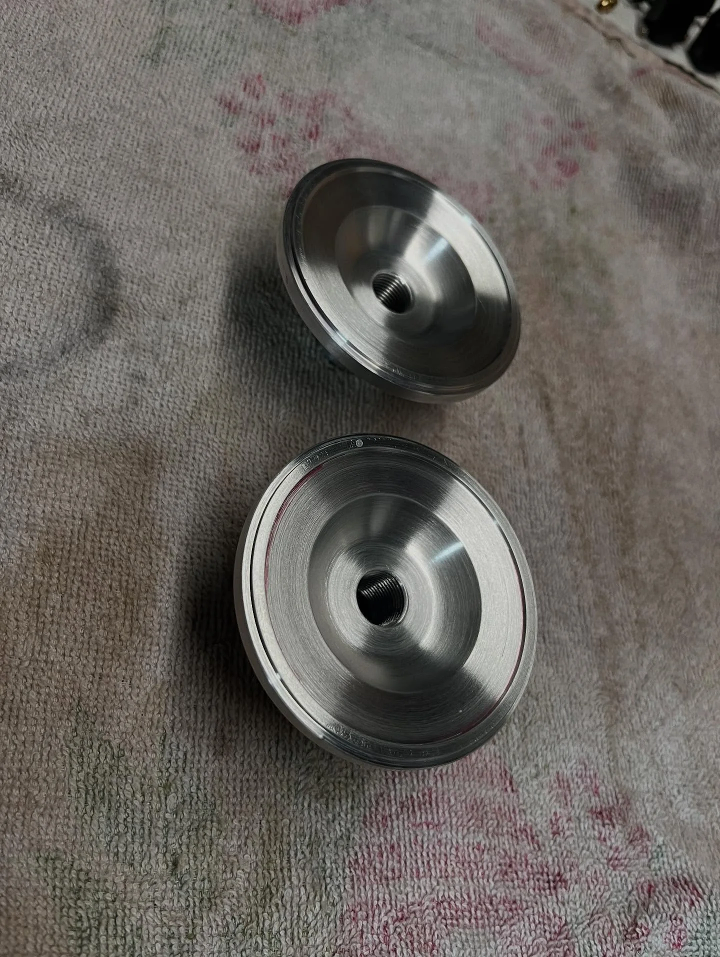 Two metal wheel hubs with threaded holes, placed on a textured fabric surface.