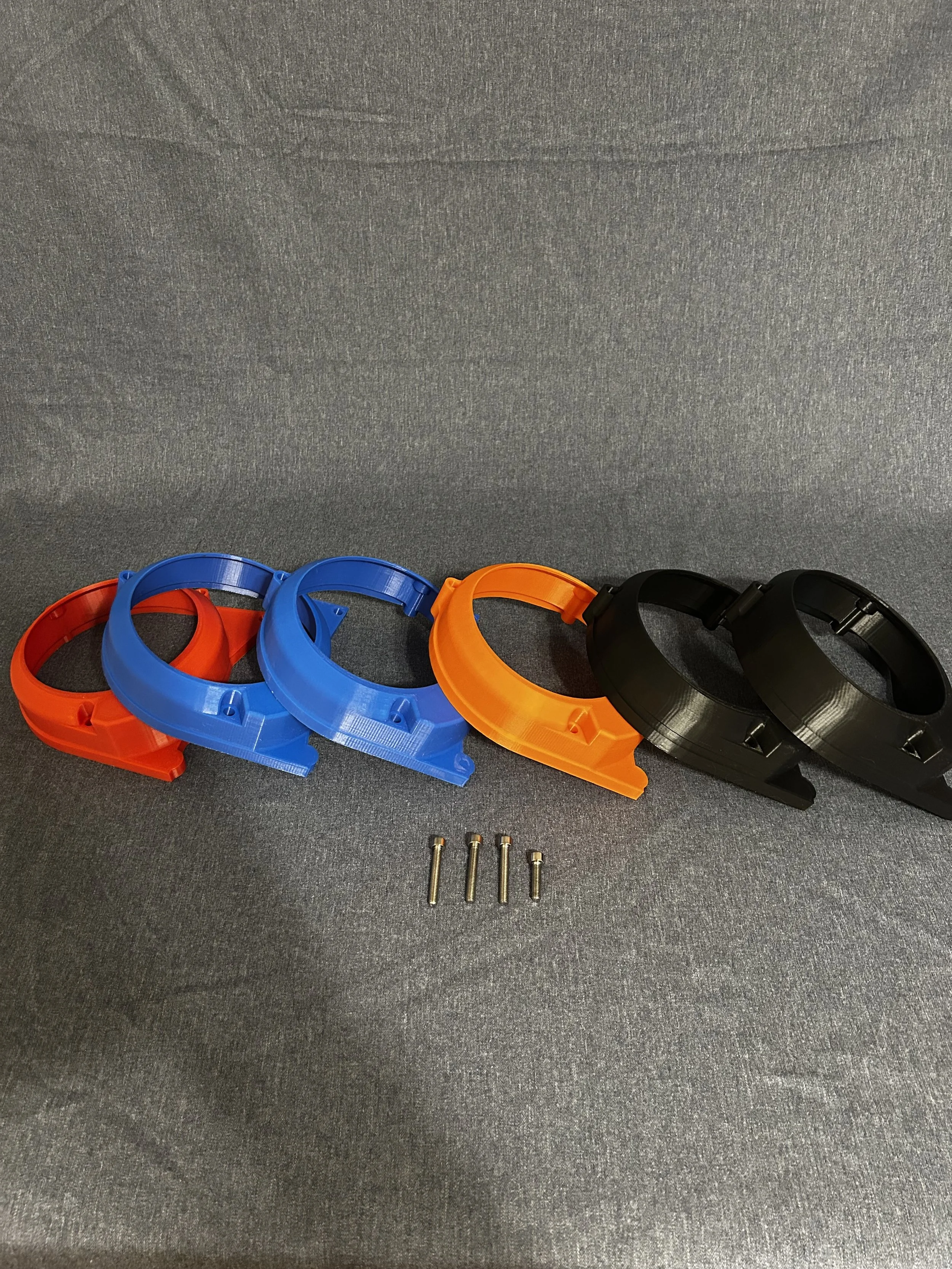 A row of colorful plastic headbands in orange, blue, yellow, and black, with four screws below, placed on a gray fabric surface.
