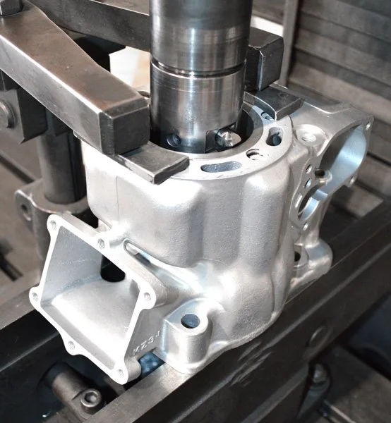 Close-up of an automotive engine component, possibly an intake manifold, mounted on a workbench with tools around it.